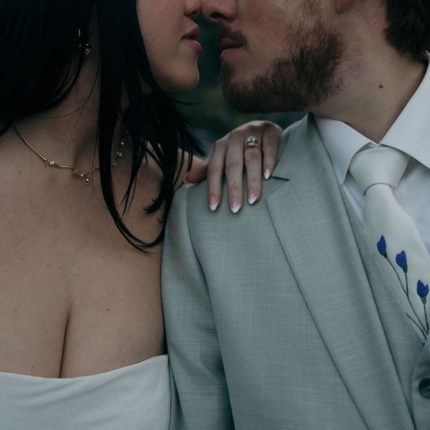 Close-up of bride and groom almost kissing, showcasing diamond engagement ring on brides hand resting on gray suit.