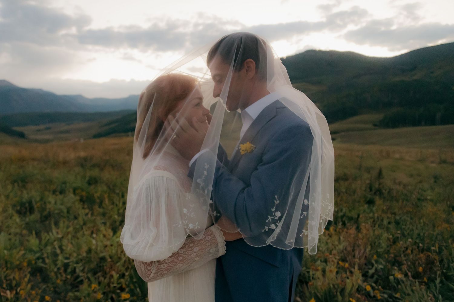 Bride and groom sharing intimate moment under wedding veil in golden mountain landscape.