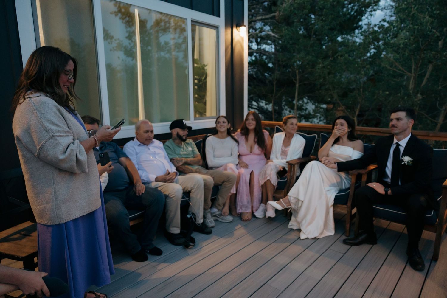Small intimate wedding ceremony on outdoor deck with guests seated while officiant speaks at dusk.