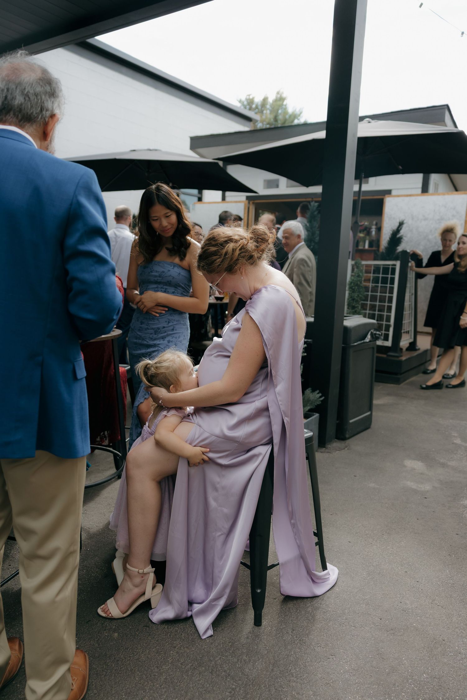 A bridesmaid in lavender gown sits with a young child on her lap at an outdoor wedding reception.