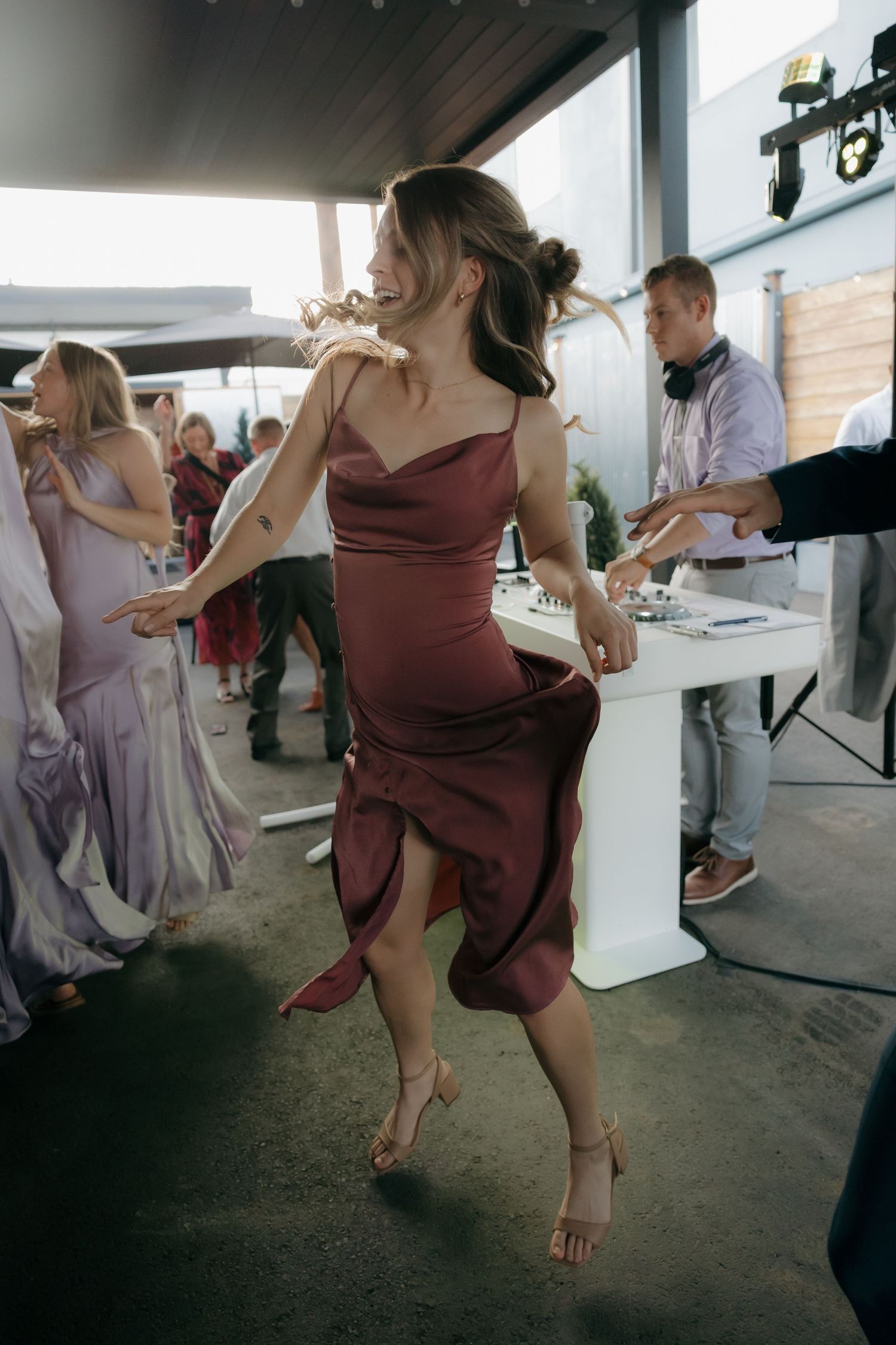 Woman in burgundy satin dress dancing joyfully at wedding reception near DJ booth.