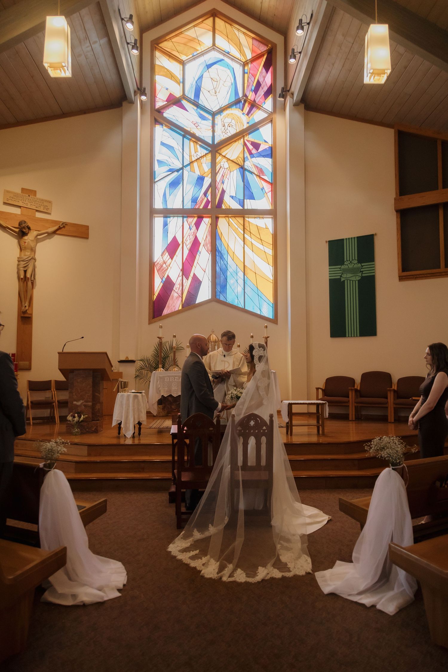 Bride and groom stand at the altar of a church with a stunning stained glass window during their wedding ceremony.