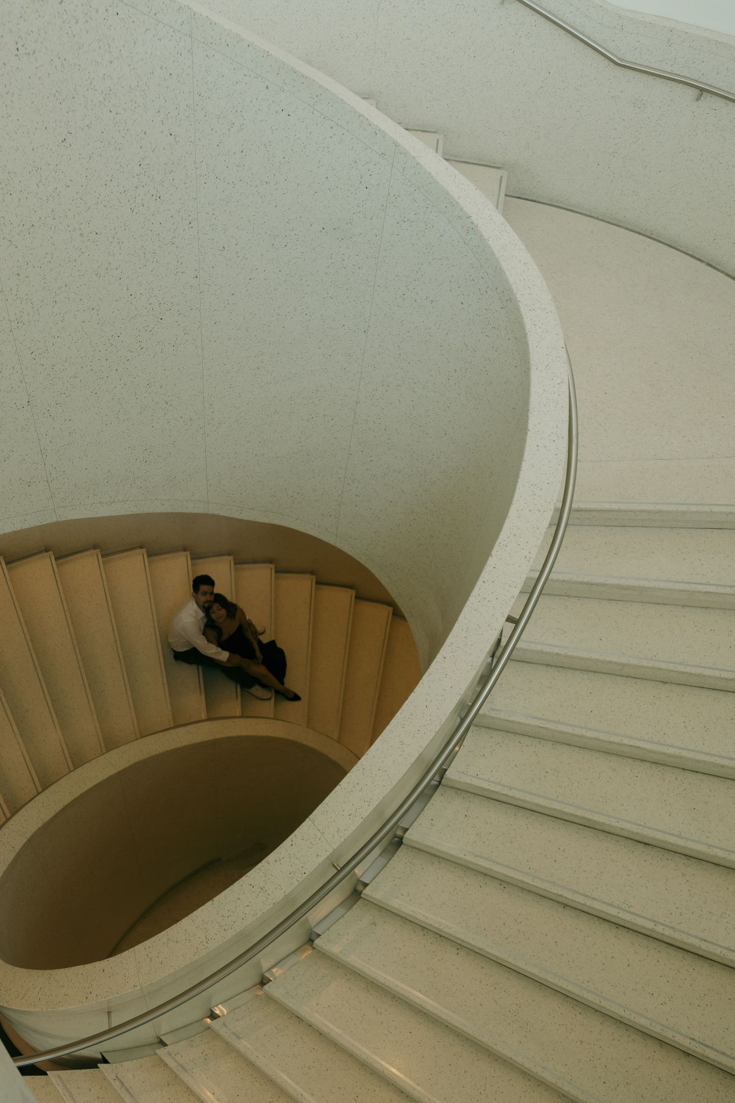 Couple sitting together at the bottom of an elegant curved spiral staircase.