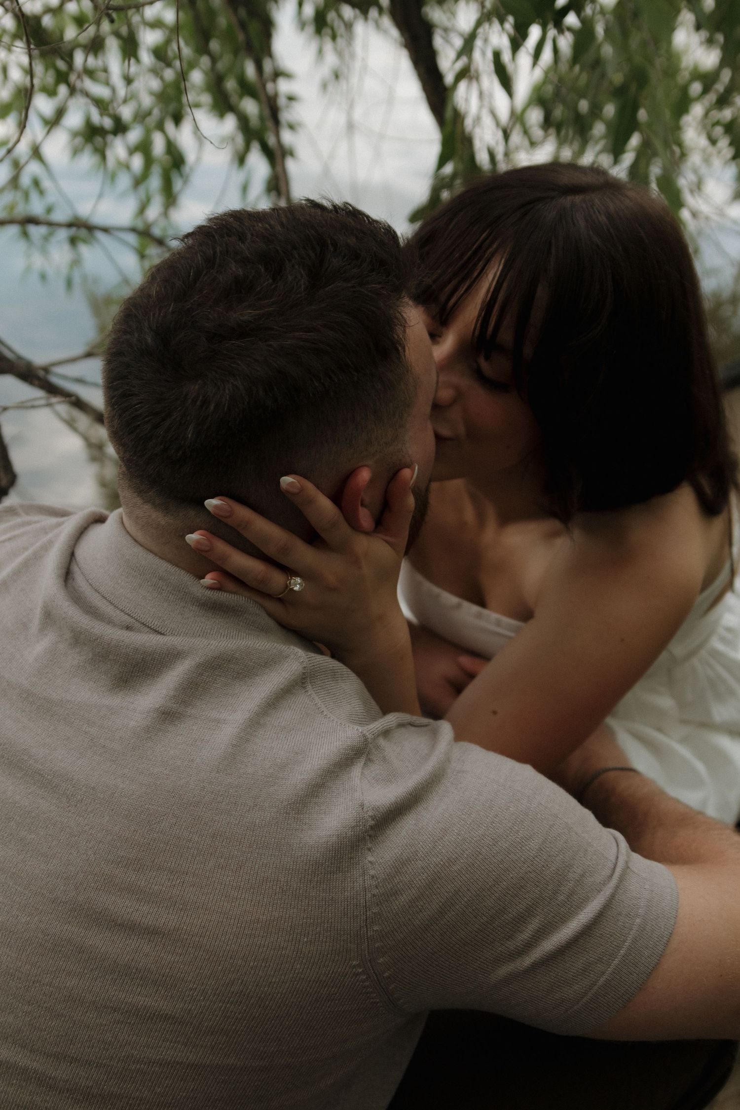 Intimate moment captured between two people in soft, natural lighting with trees in background.