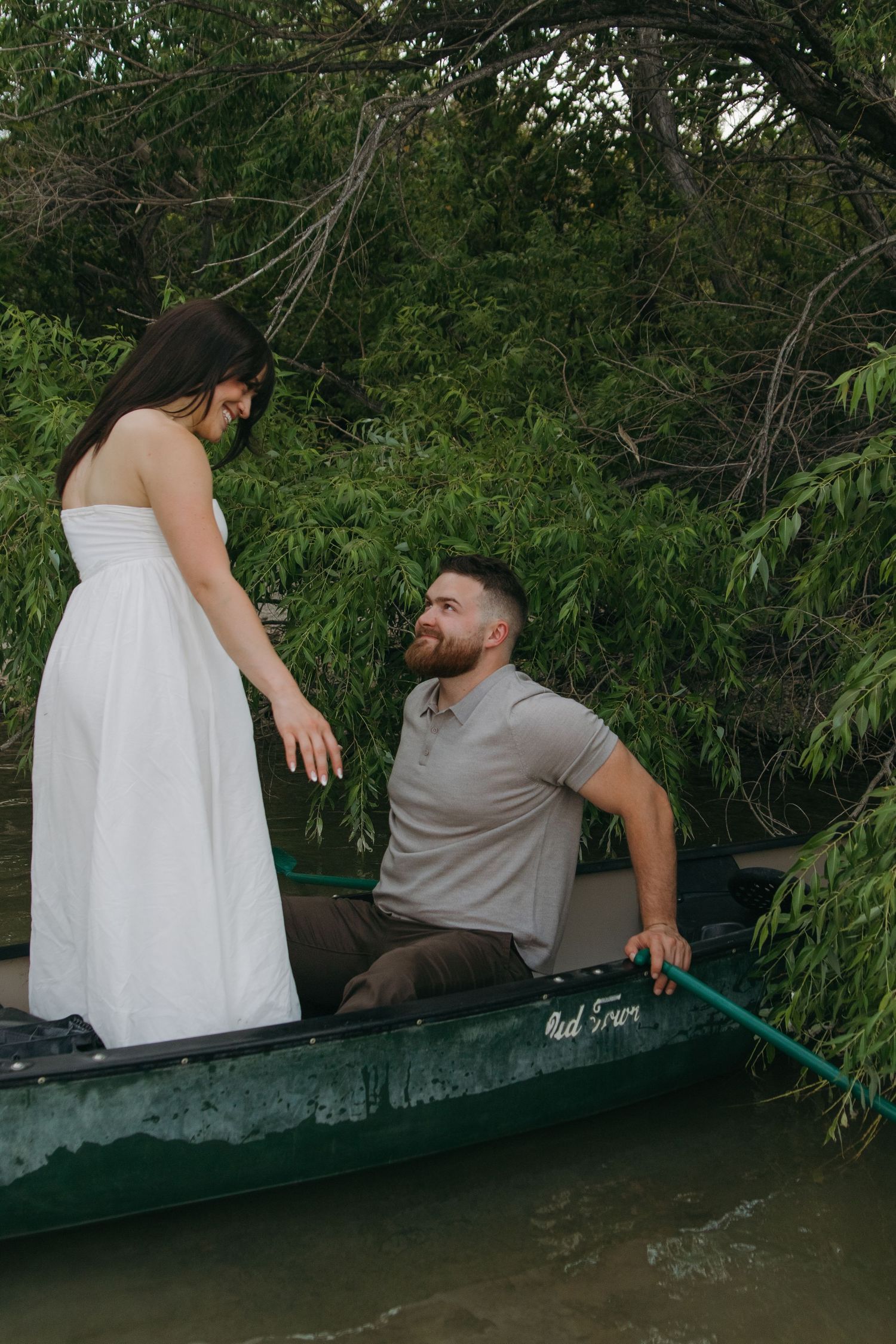A couple shares a tender moment while sitting in a green canoe surrounded by lush foliage.