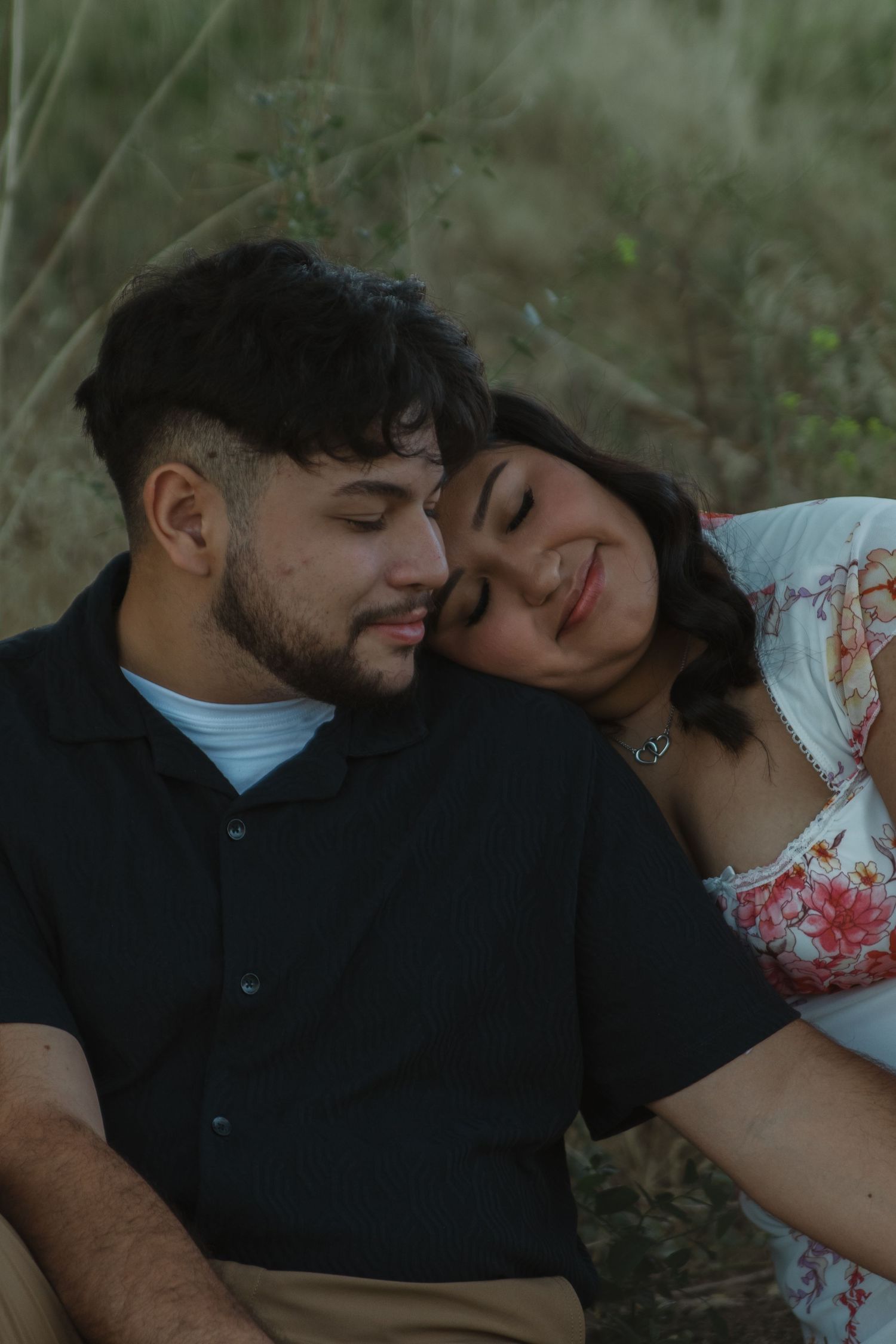 A couple rests their heads together while sitting in nature during sunset.
