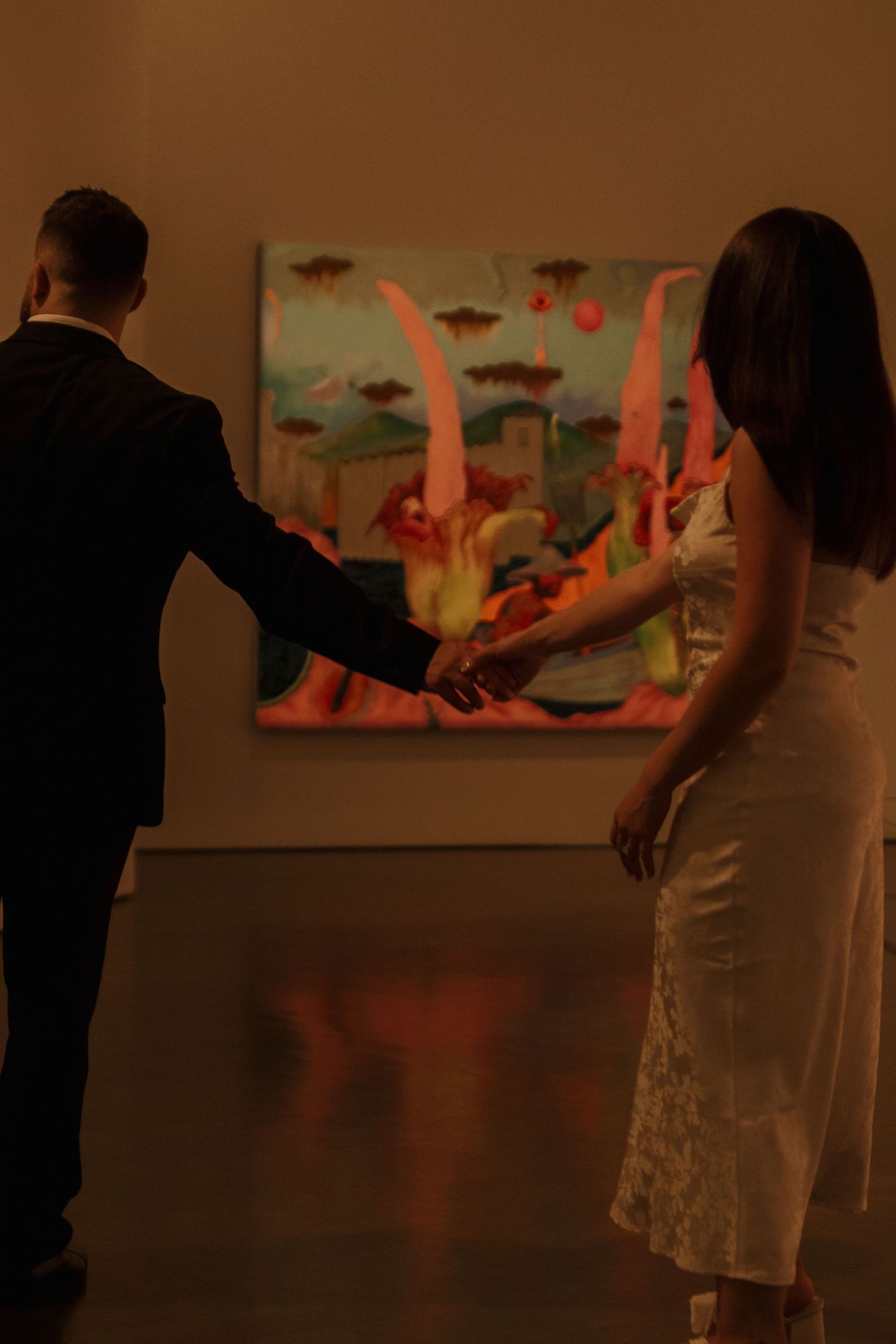 Two figures engage in an intimate dance pose against a dimly lit artistic backdrop with pink accents.
