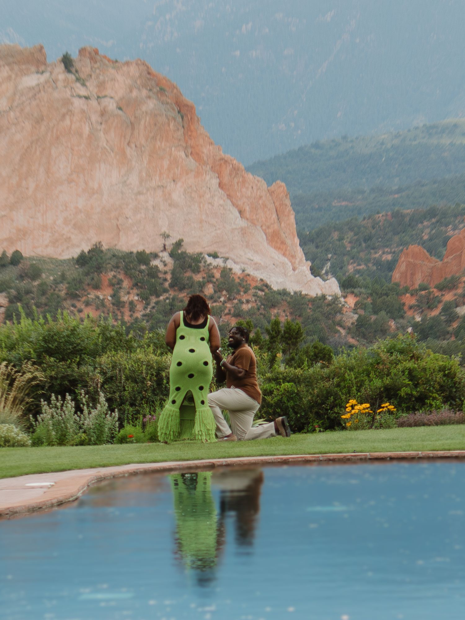 A serene pool reflects the majestic red rocks of Garden of the Gods in Colorado Springs with people enjoying the view.
