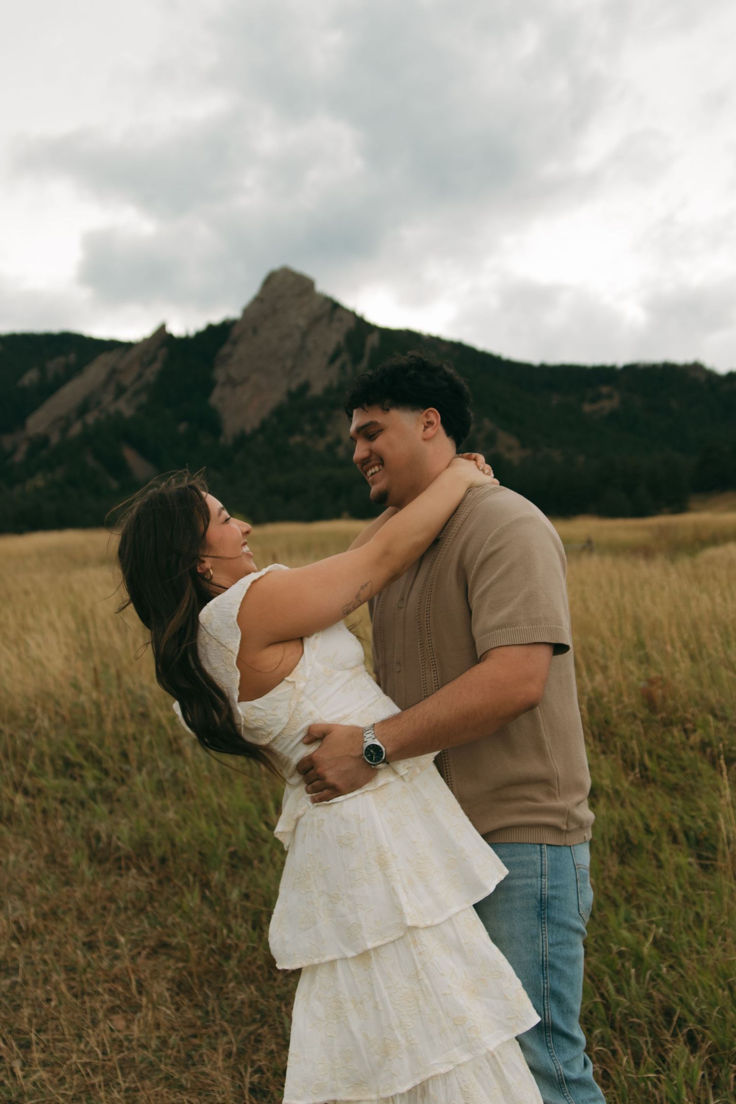 Romantic couple laughing together in grassy field with stunning Colorado Flatirons mountains behind.