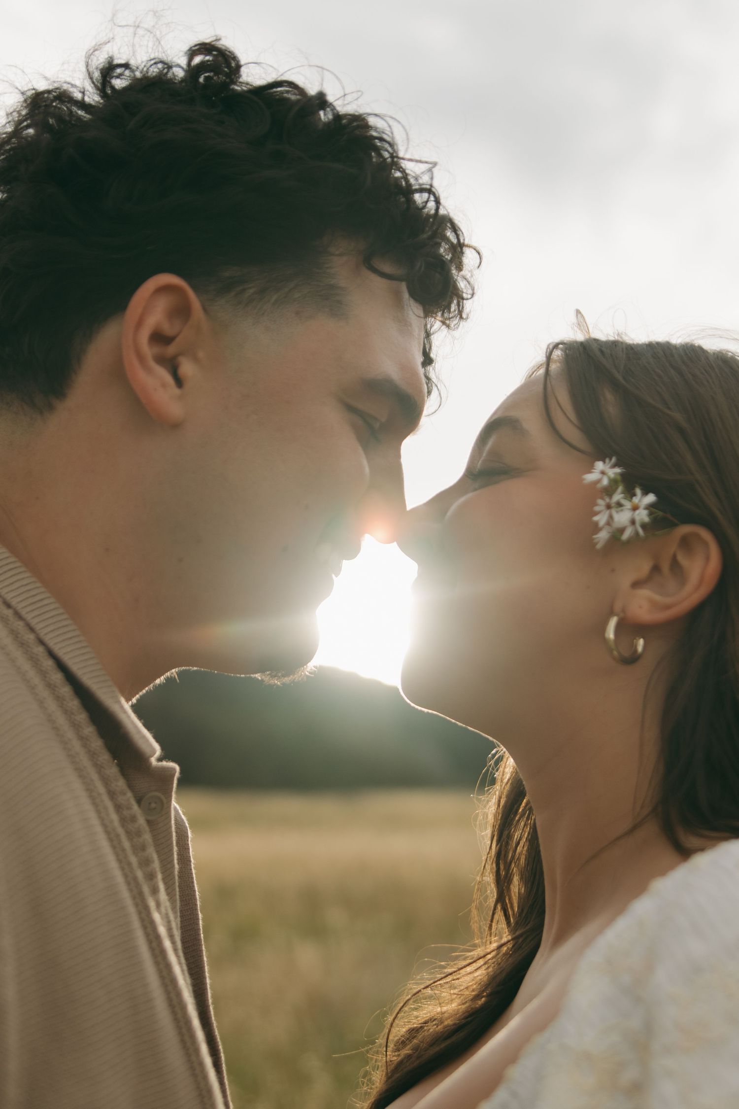 Close-up of couple about to kiss with golden sunlight glowing between them outdoors.