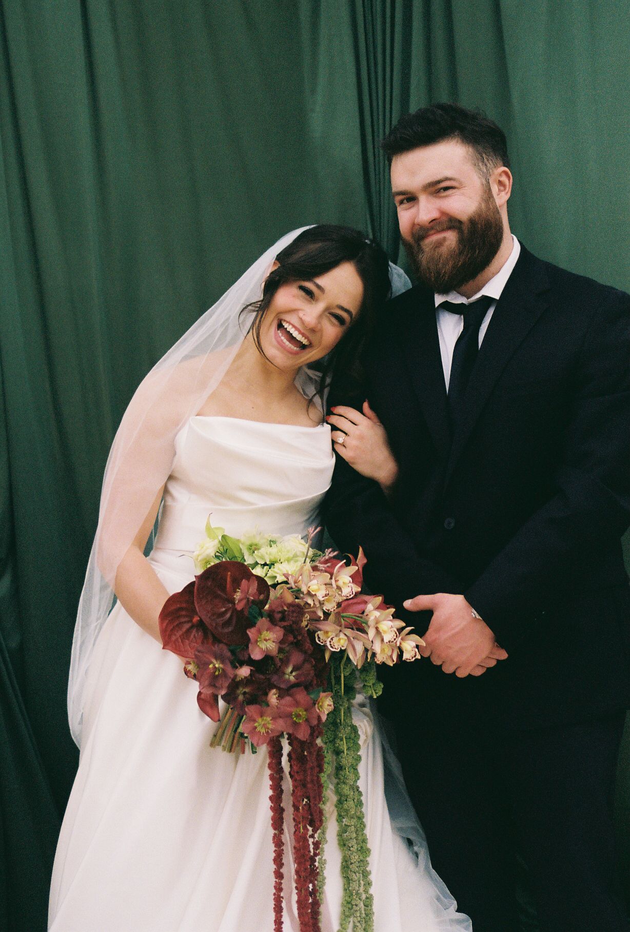A happy couple shares joyful moments against a green backdrop during their wedding photoshoot.