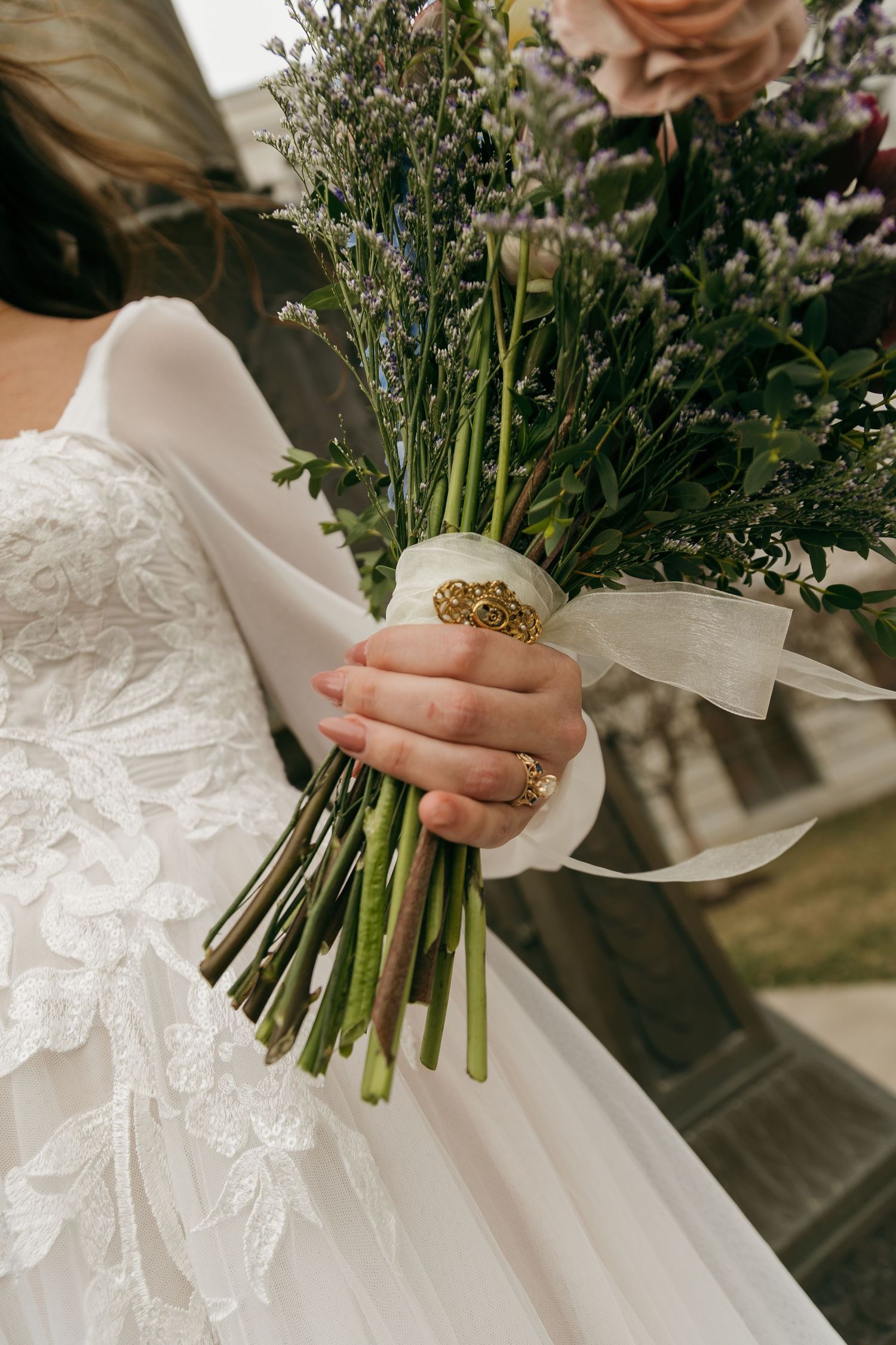 Close-up of wedding bouquet with roses and greenery held by hands in white lace.