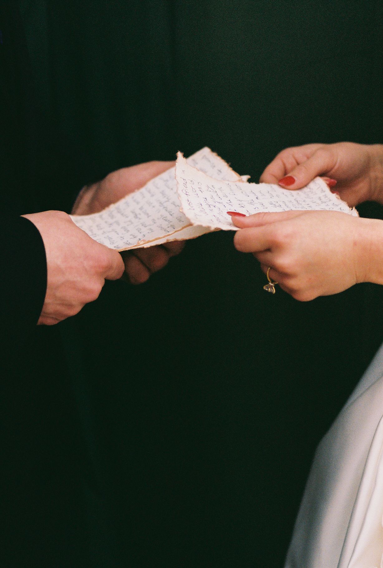Hands exchanging wedding vows or letters in a sequence of artistic black and white shots.