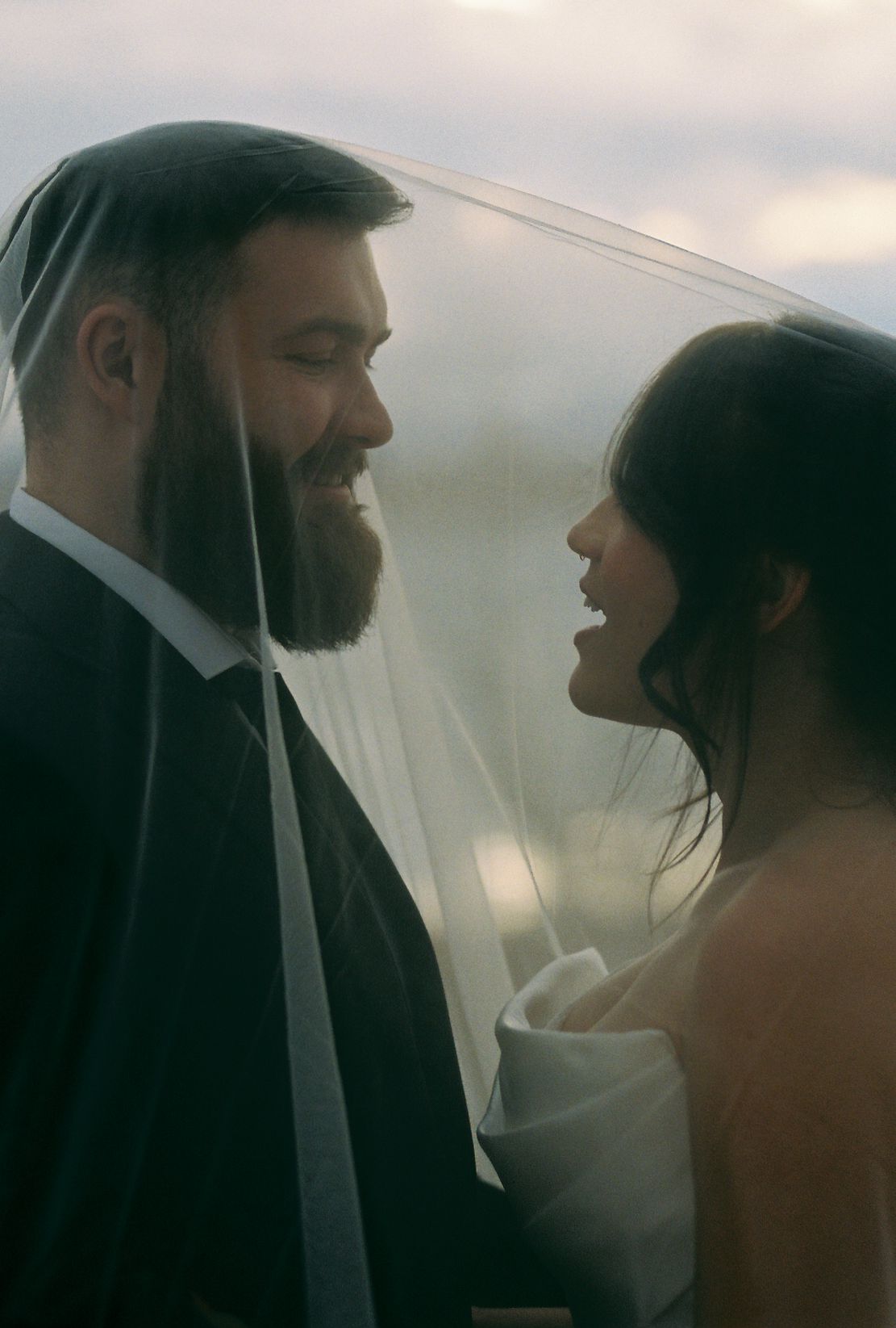 A tender moment captured under sheer bridal veil with soft natural lighting.