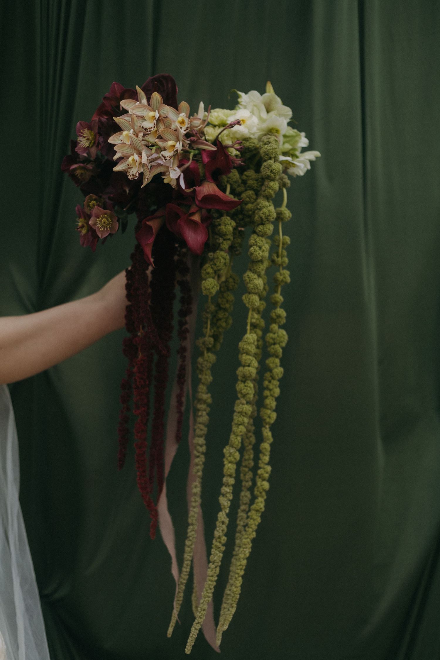 Cascading yellow and burgundy floral arrangements hang against a dark green backdrop.