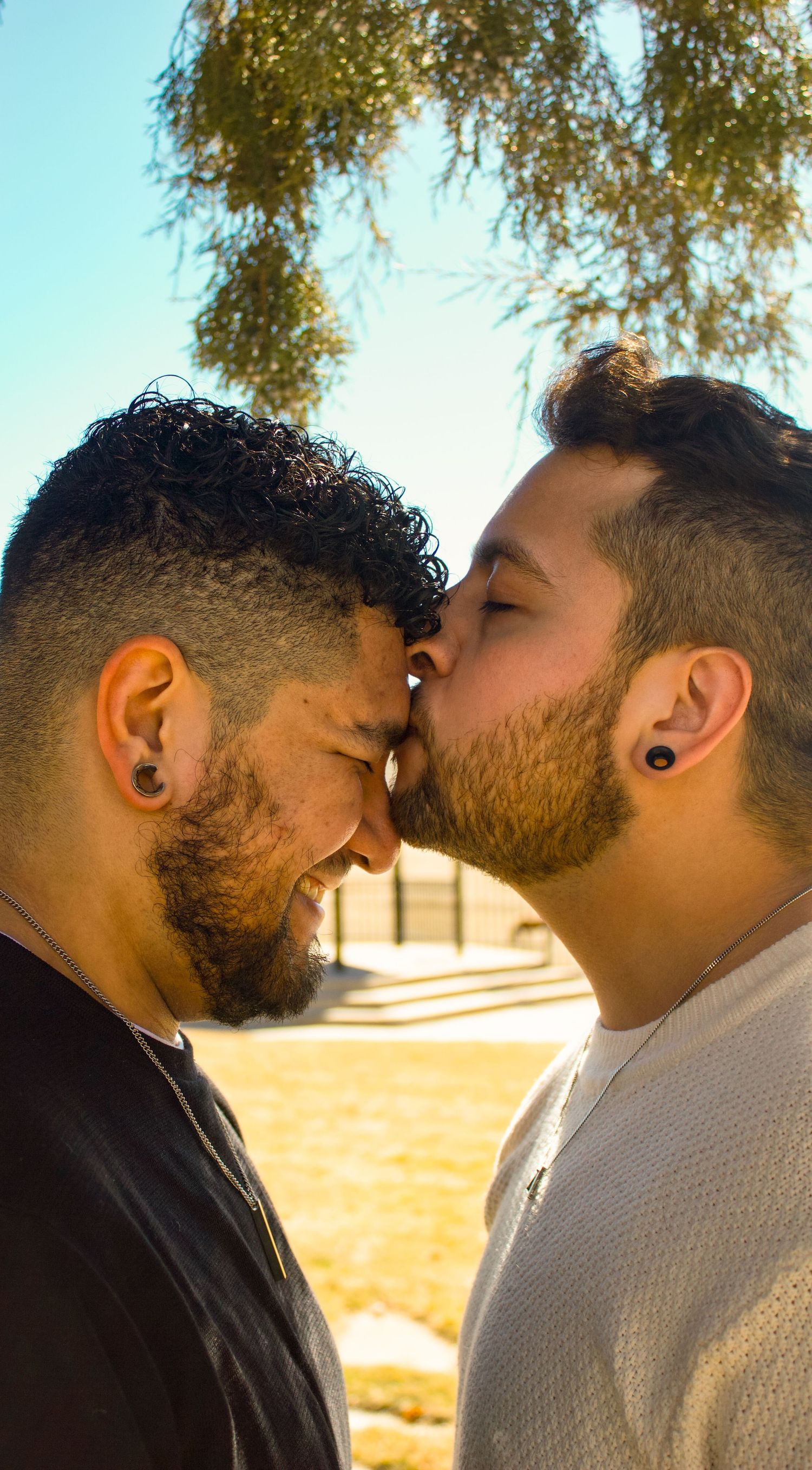 Tender embrace captured in portrait orientation with blue sky and trees in background.