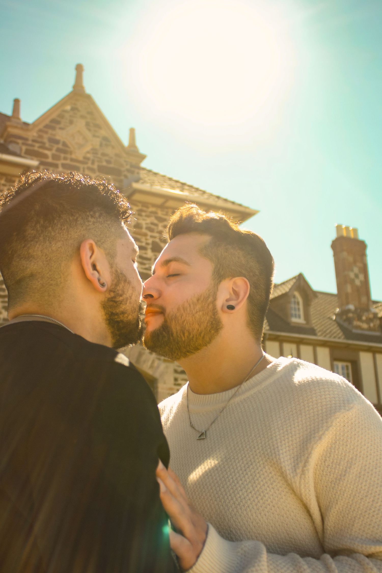 Couple sharing tender moment outdoors with stone building facade visible in background.