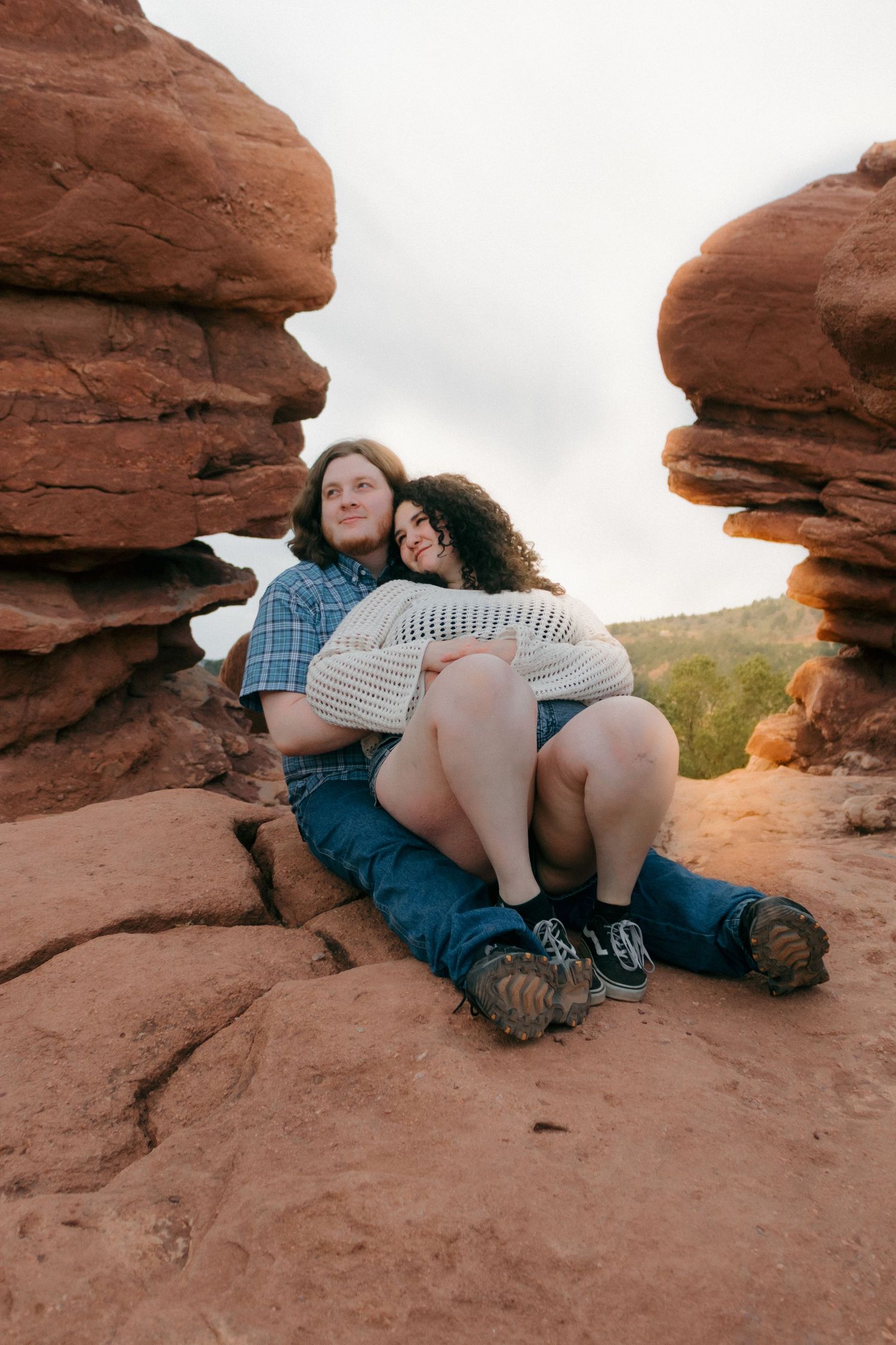 Two people cuddle on red rocks while sitting between natural stone formations.
