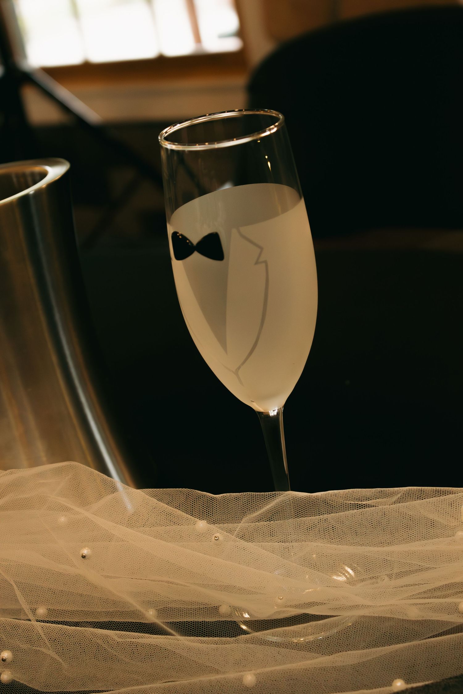 Decorative champagne glass with bow tie design silhouette against white tulle fabric.