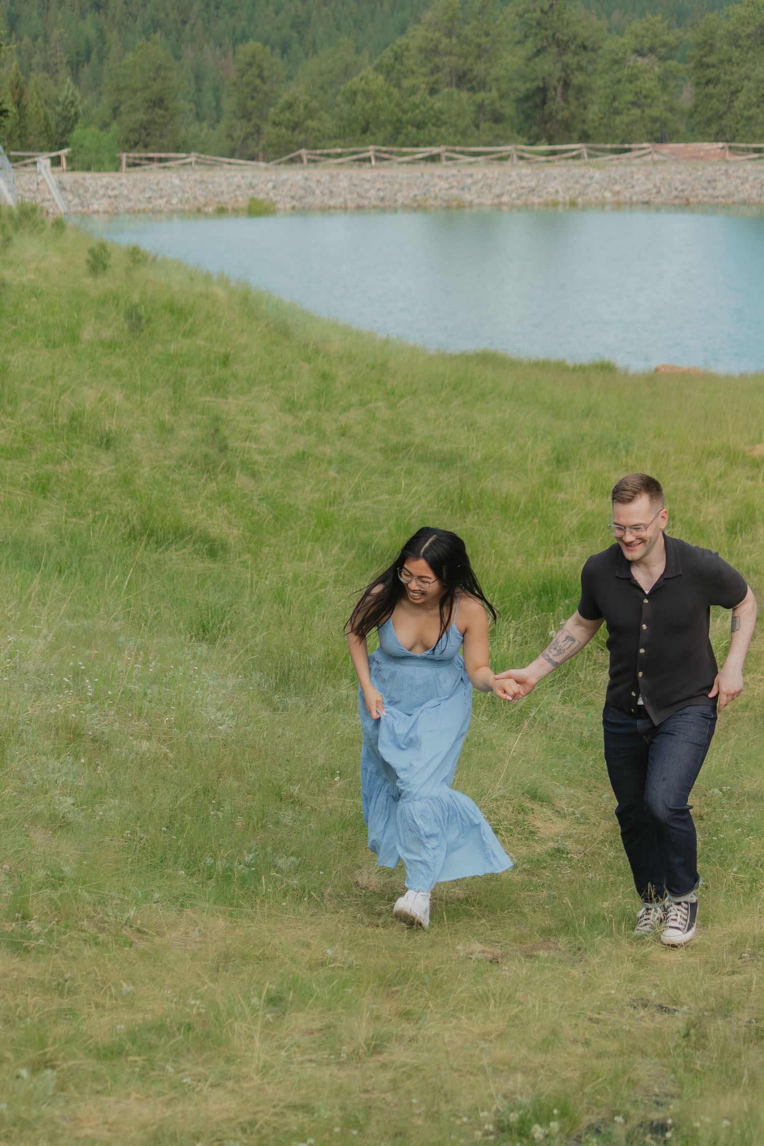 Couple running and playing on a grassy hillside near a lake during a photo session.