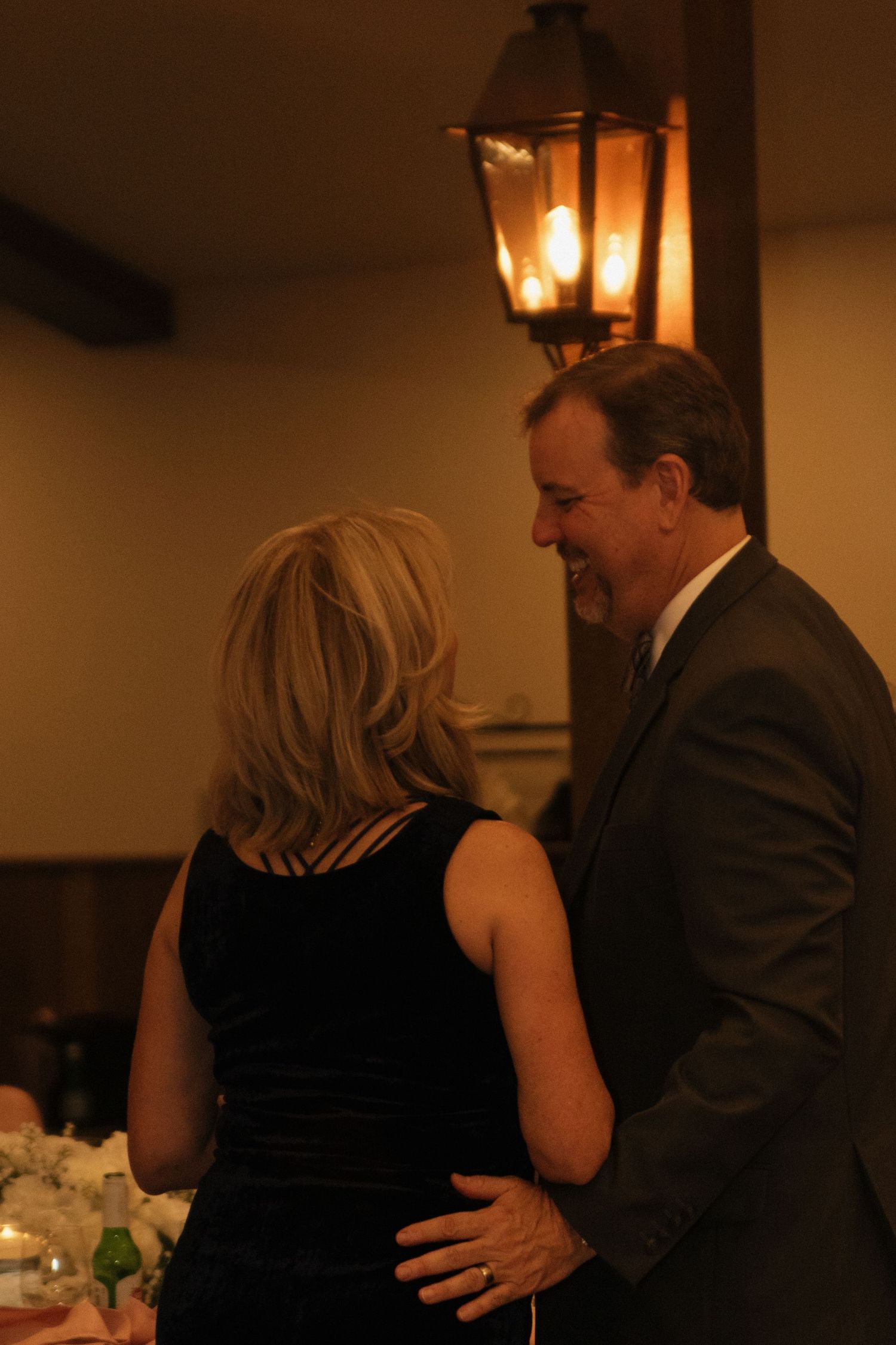 Couples slow dancing at a wedding reception under warm ambient lighting.