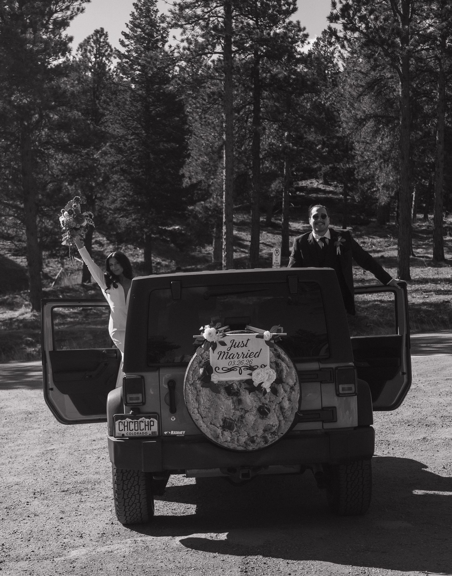 Newlyweds celebrate beside decorated Just Married Jeep in black and white forest wedding photo.