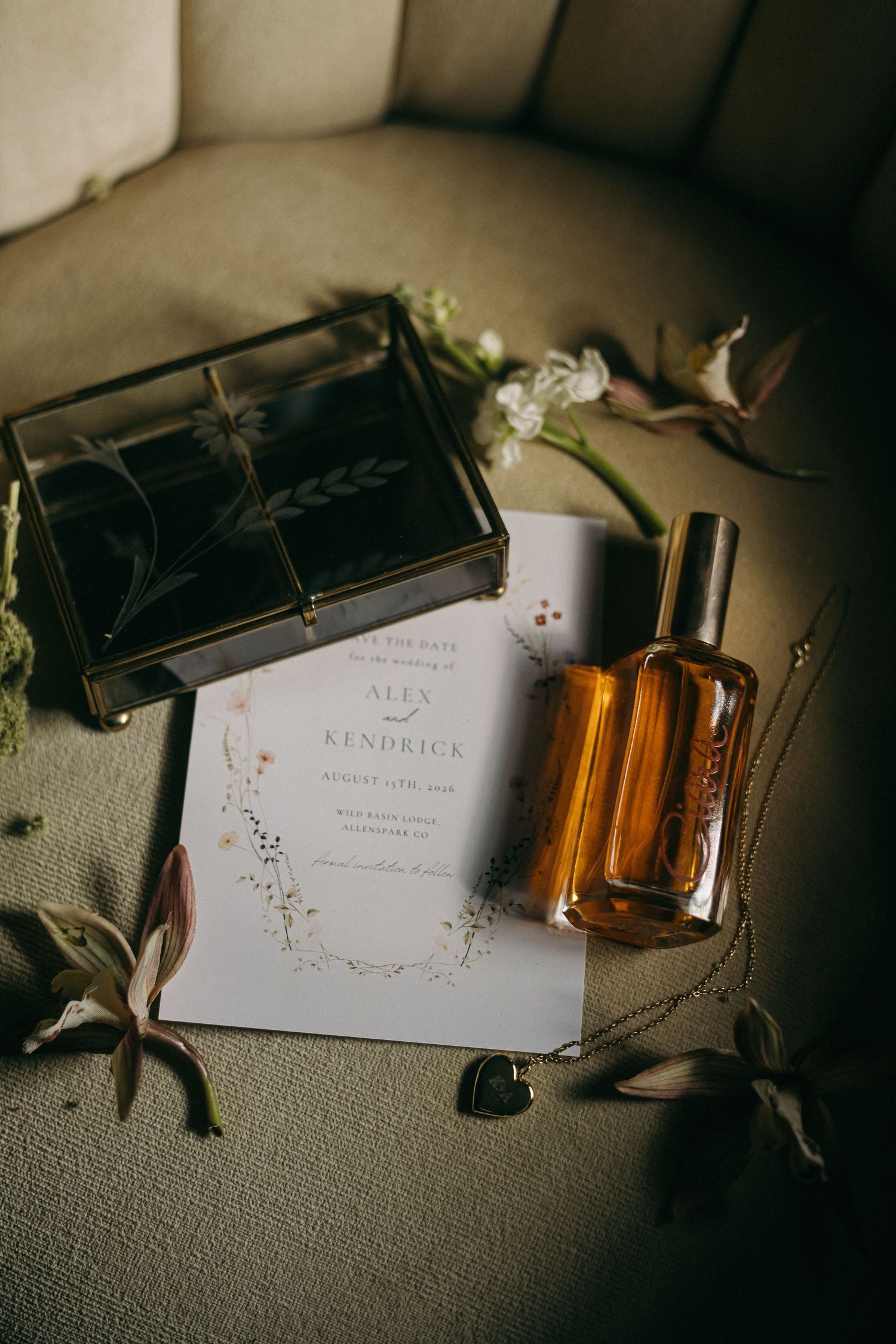 Wedding invitation cards and perfume bottles arranged artistically in moody lighting on a textured surface.