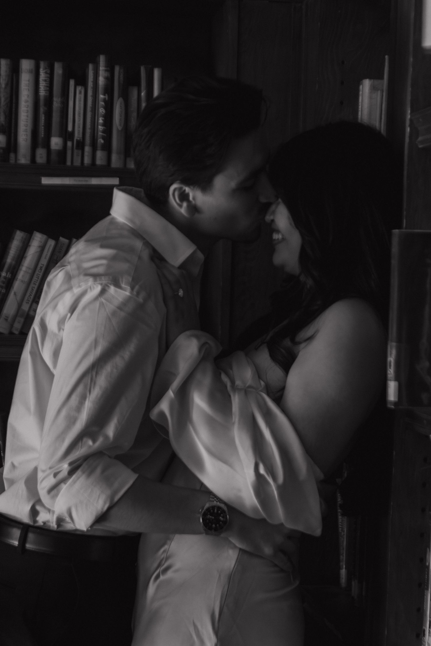 An intimate black and white photo of a couple embracing in a library setting.