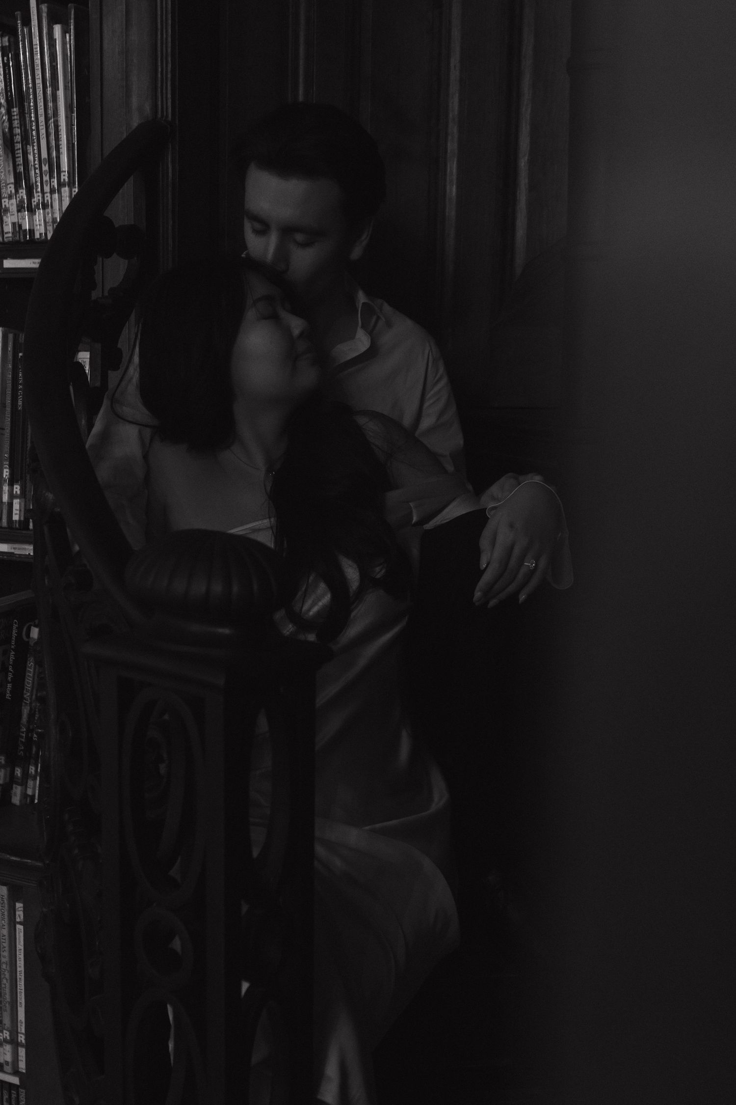 Atmospheric black and white photo of couple between library shelves.