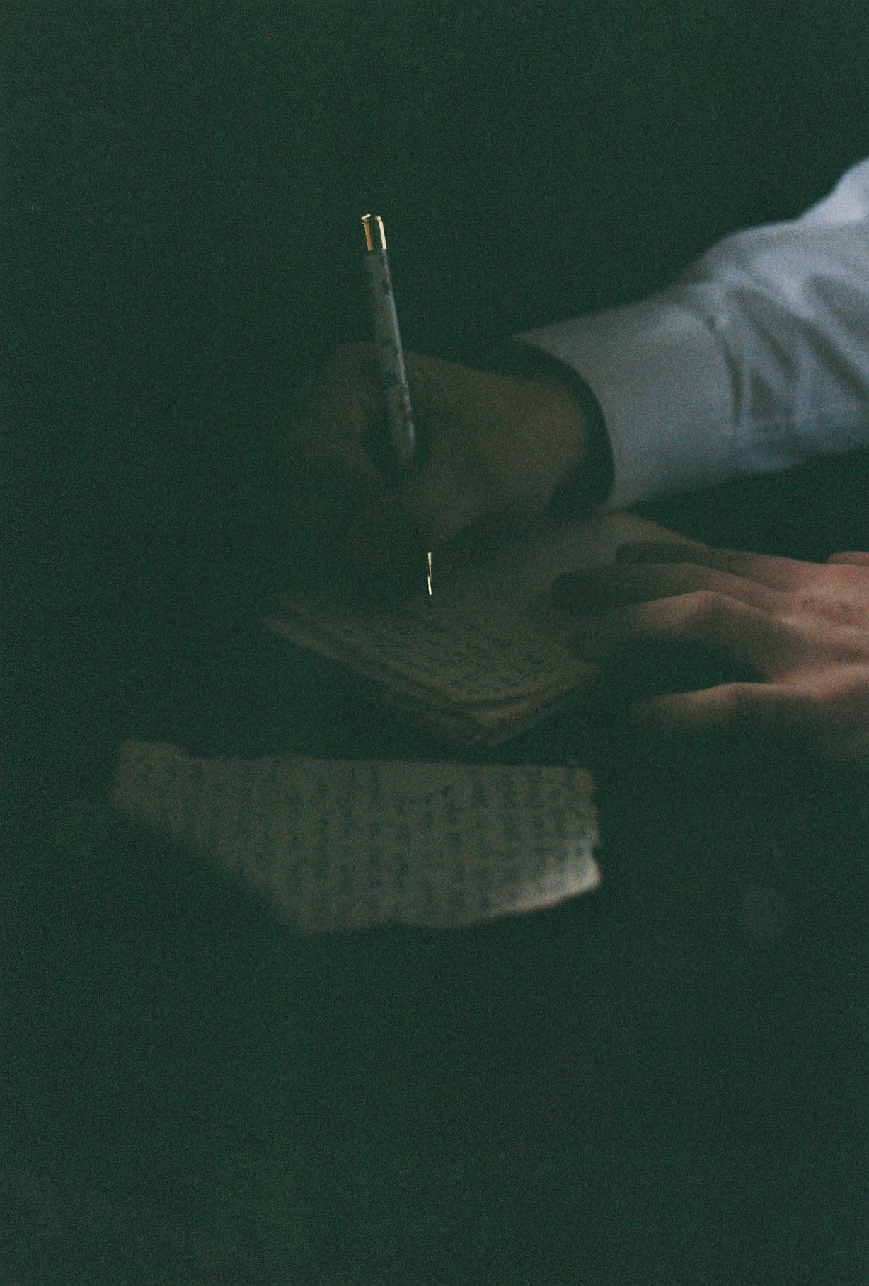 Atmospheric dark photo of hands writing on paper with fountain pen.