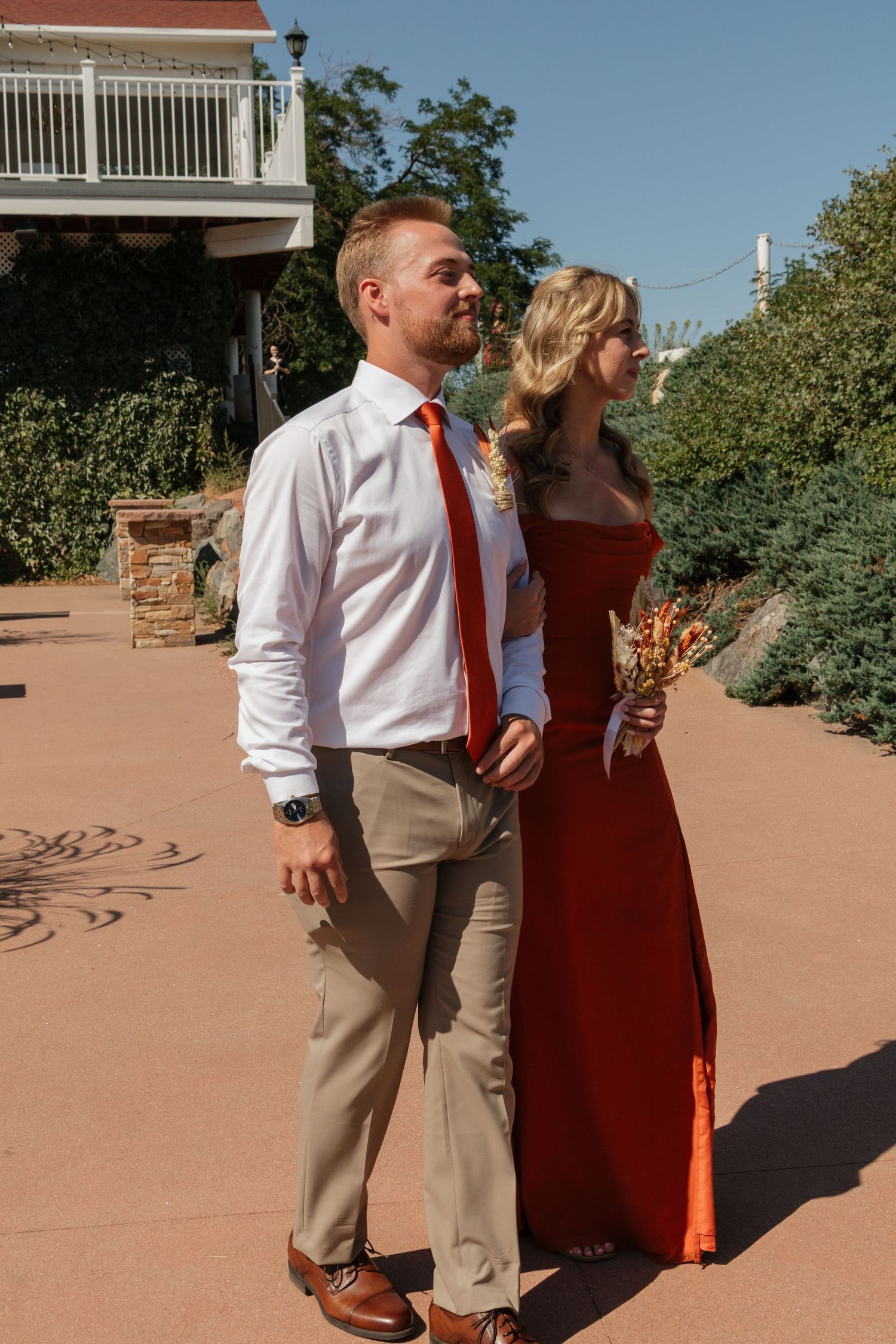 Wedding party members in red and khaki attire pose against a desert landscape setting.