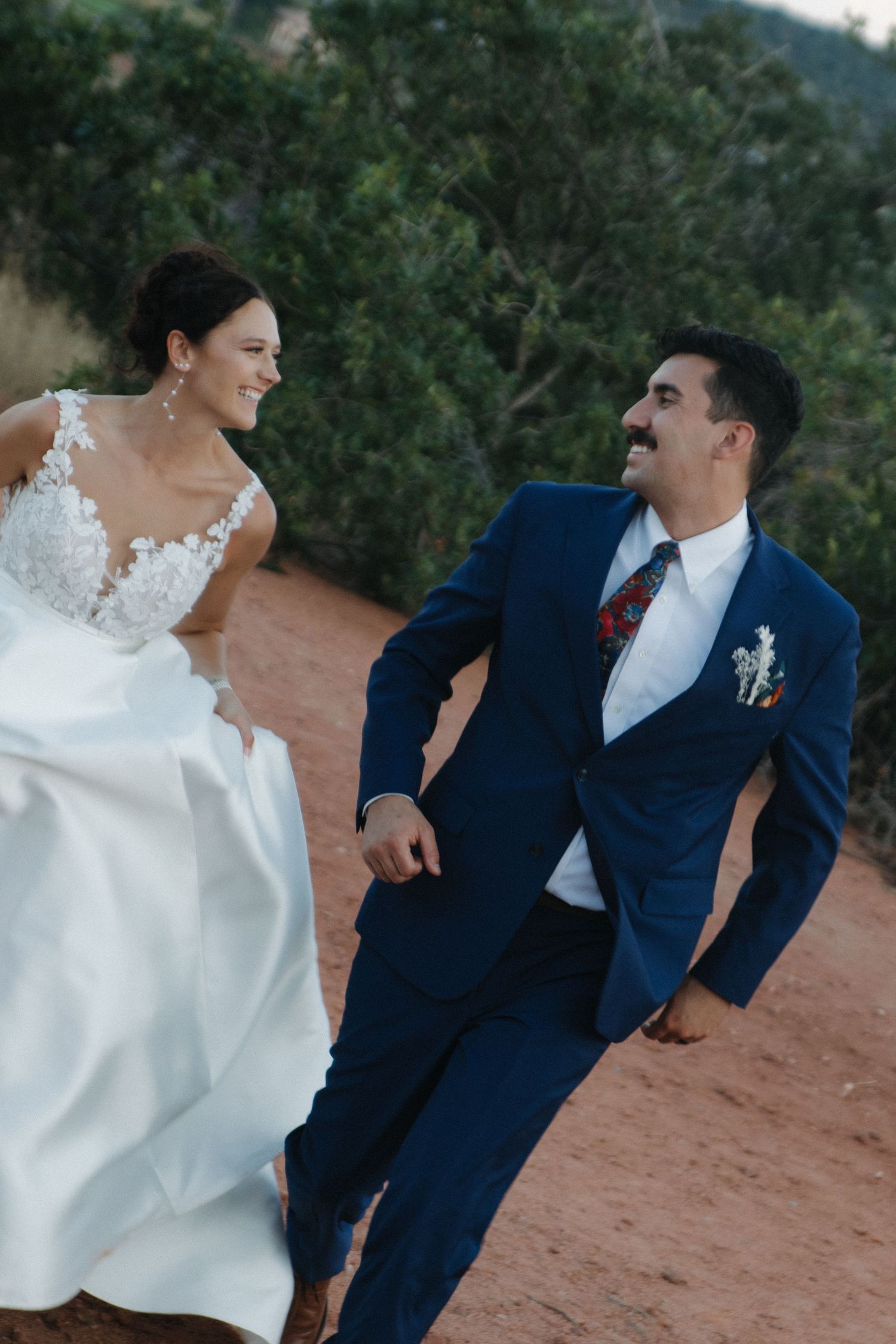Joyful wedding couple laughing together outdoors against natural landscape.
