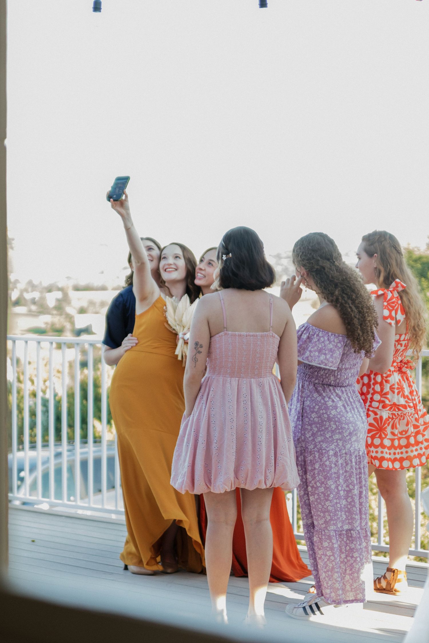 Group of people in colorful summer dresses enjoying a moment on an outdoor deck.