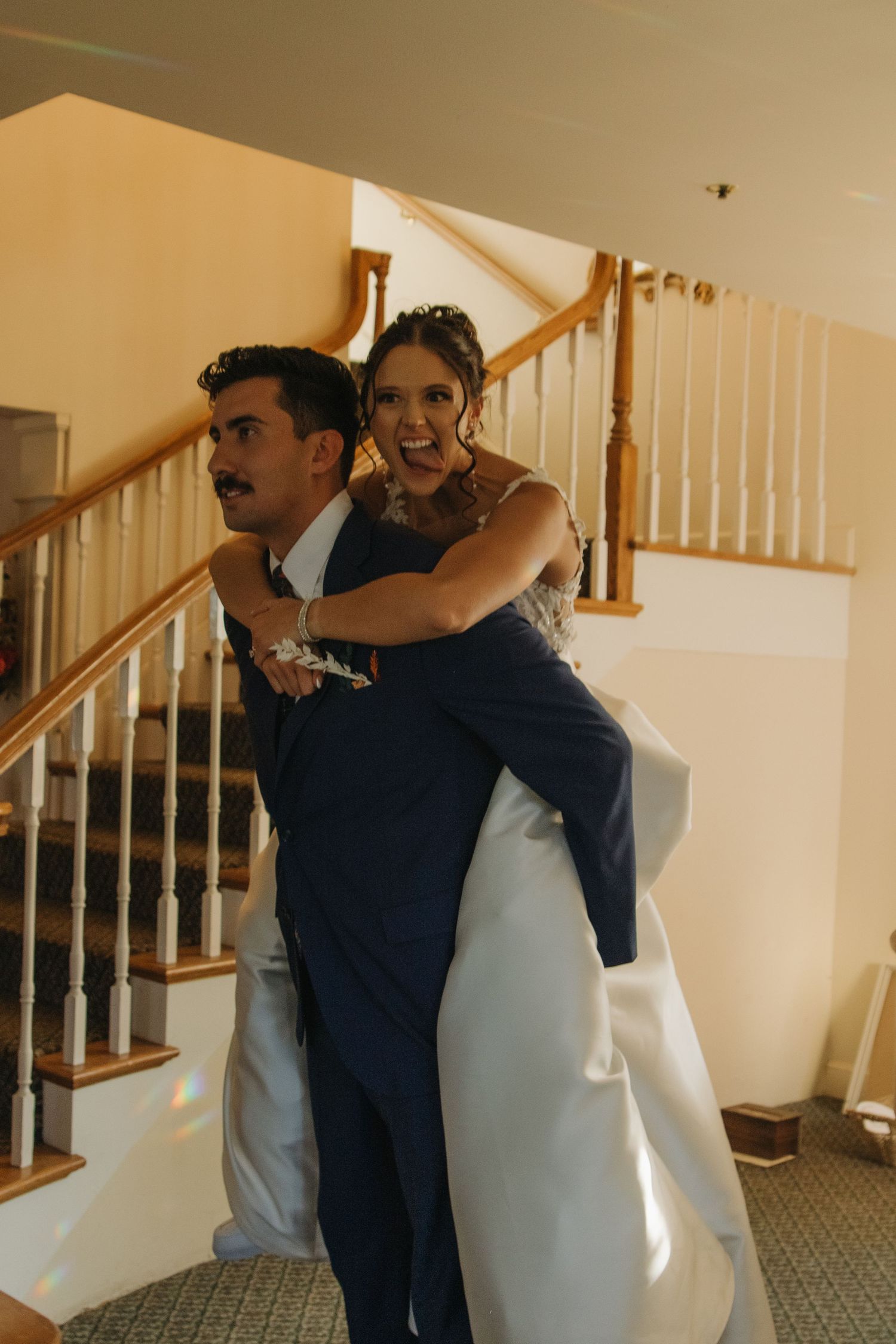A tender moment between two people in formal attire by a white staircase with wooden railings.