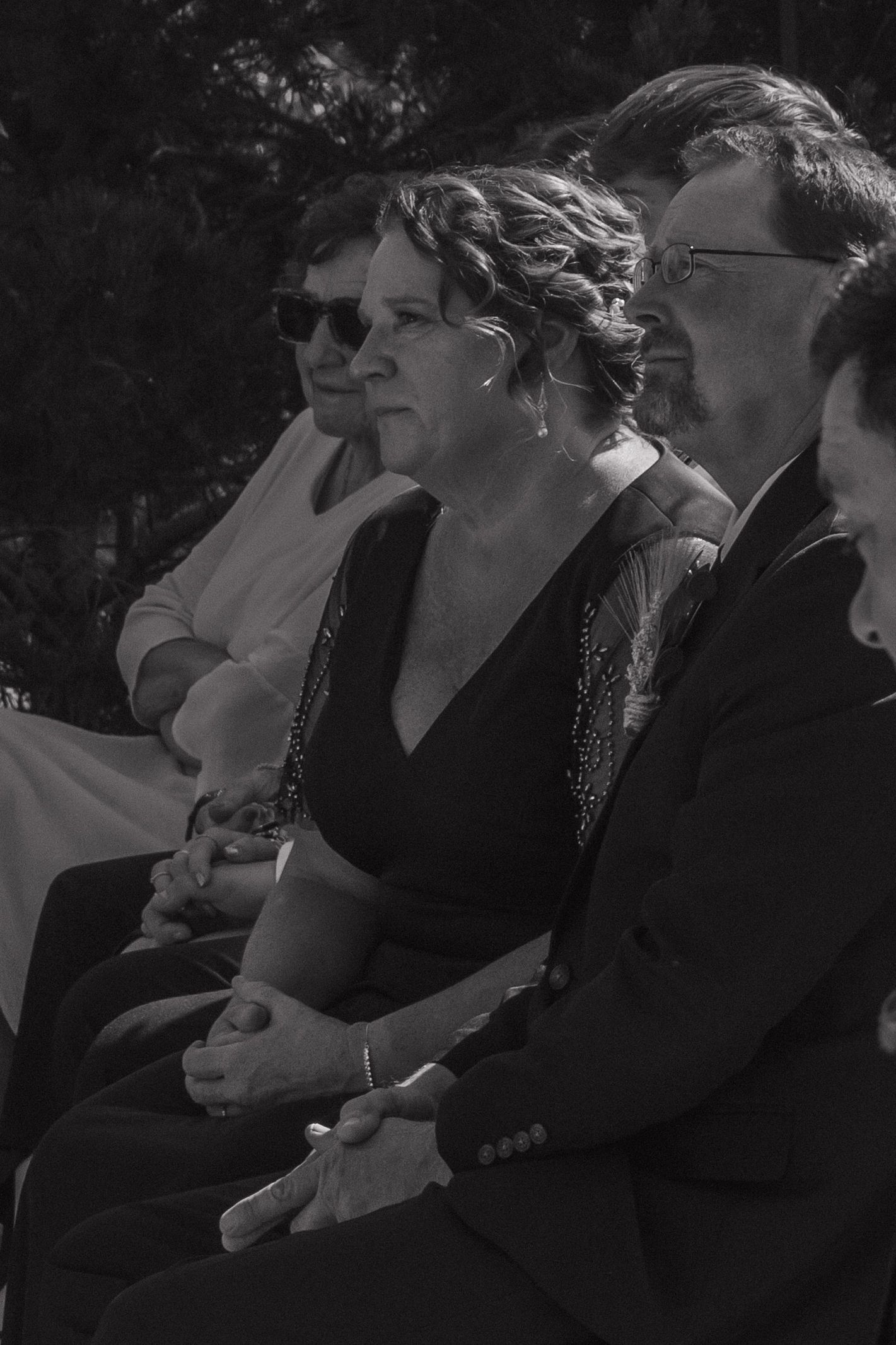 Wedding guests seated in black attire watching the ceremony outdoors.
