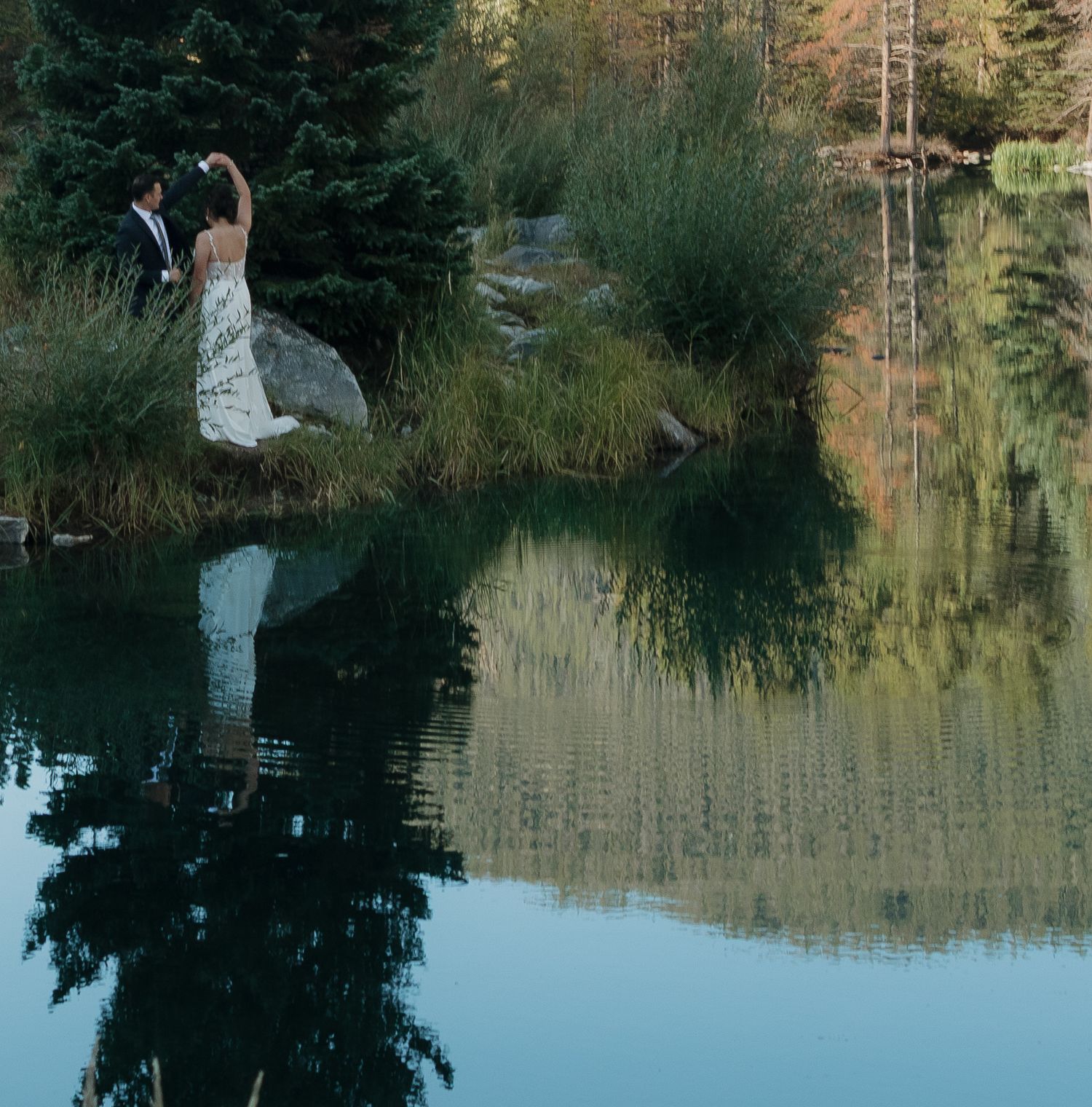 Serene lake reflections with pine trees and mountains creating a mirror-like effect.