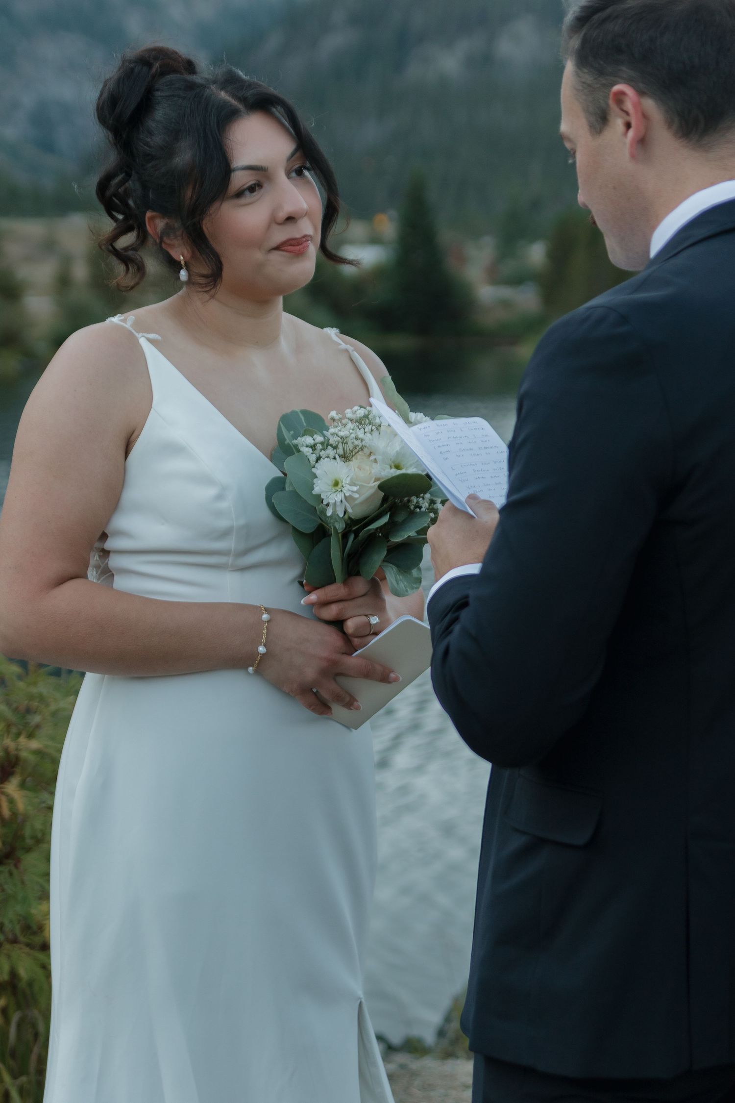 Wedding ceremony details showing someone holding a bouquet and exchanging vows by the water.