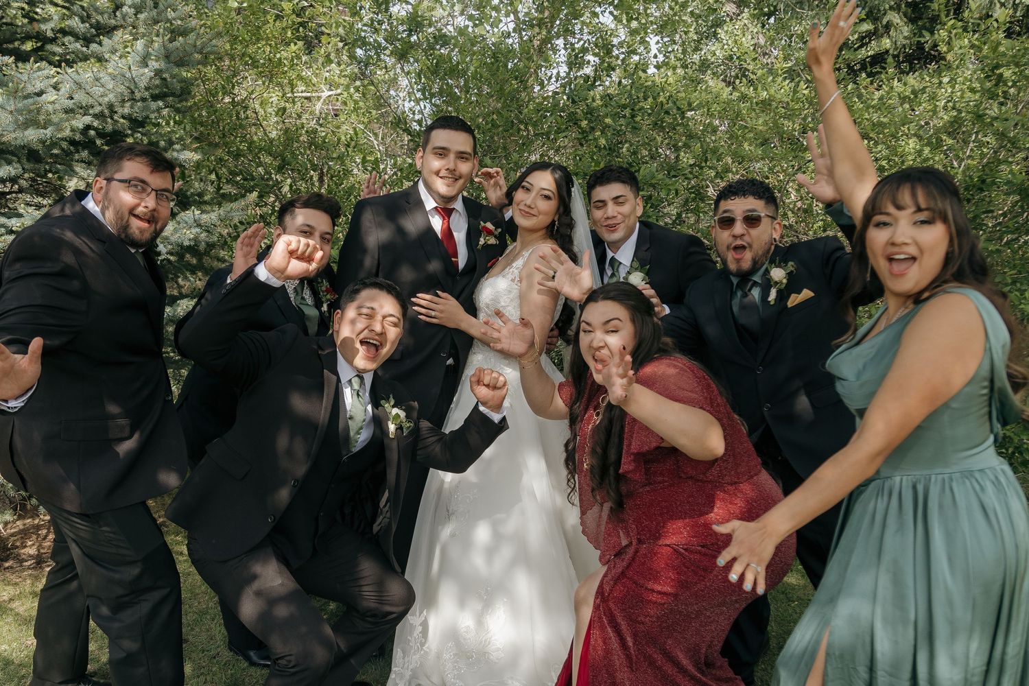 Joyful wedding party celebrates outdoors with bride and groom surrounded by groomsmen and bridesmaids in blue and red.