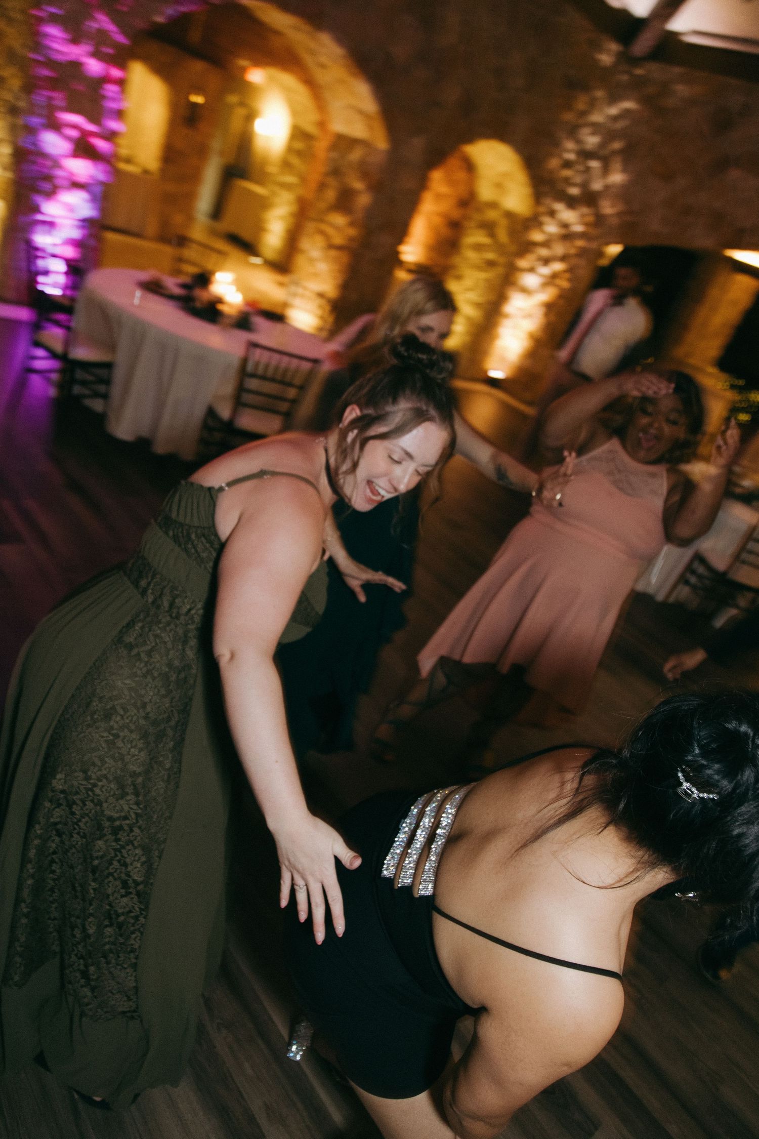 Wedding guests dancing and laughing enthusiastically in a stone-walled reception venue.