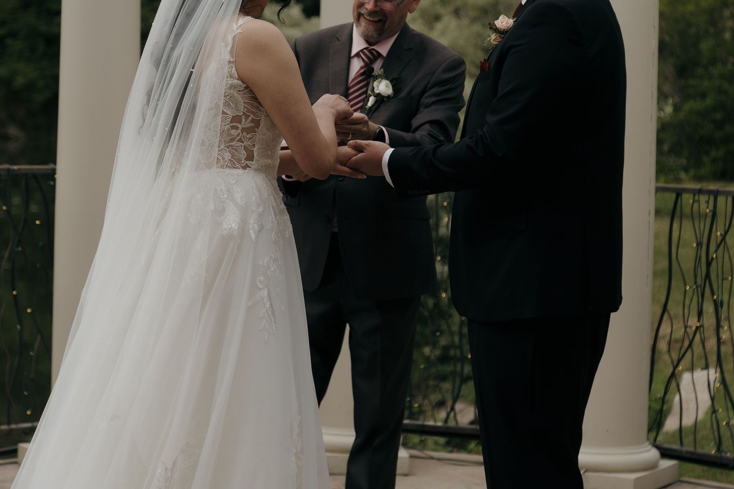 Bride and groom hold hands during intimate wedding vow exchange with officiant between white columns.