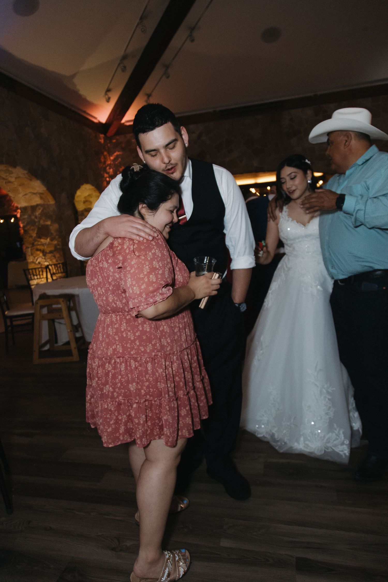 Groom dances with a family member while bride dances with another guest at wedding reception.