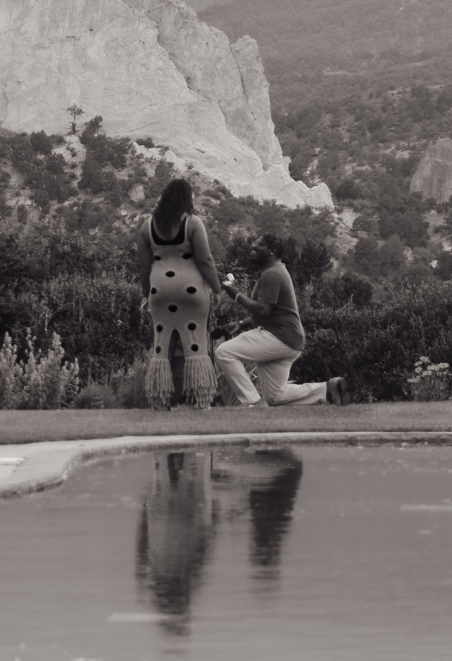 A romantic proposal moment captured in black and white next to a reflective pool with dramatic white cliffs in the background.