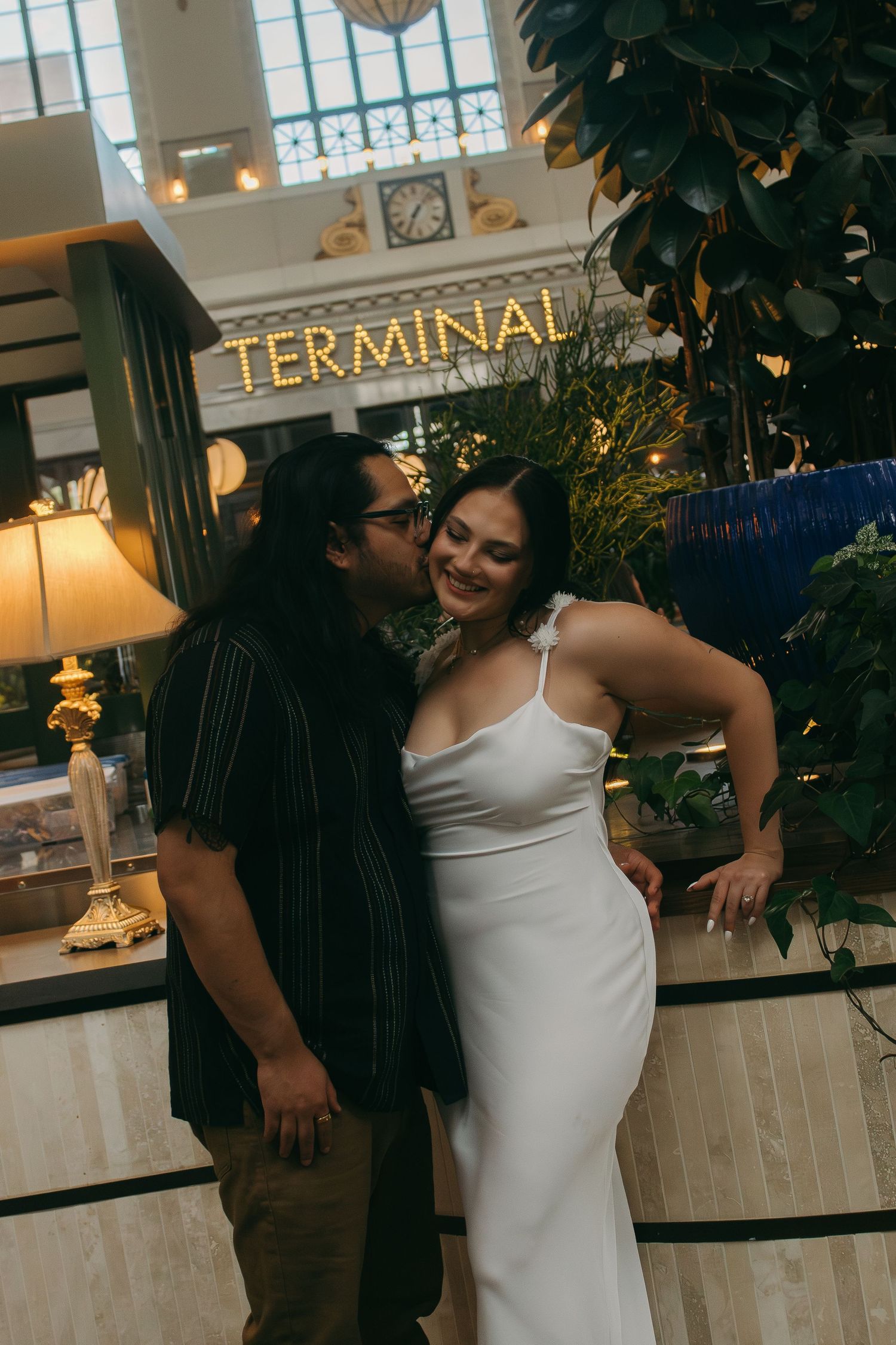 A couple embraces in front of a terminal sign in a historic building interior.