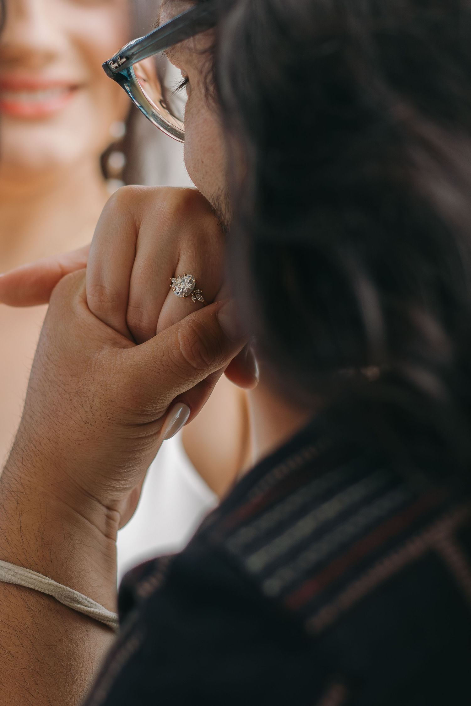 Close-up view of someone wearing an engagement ring with a sparkling diamond in a soft, warm lit setting.