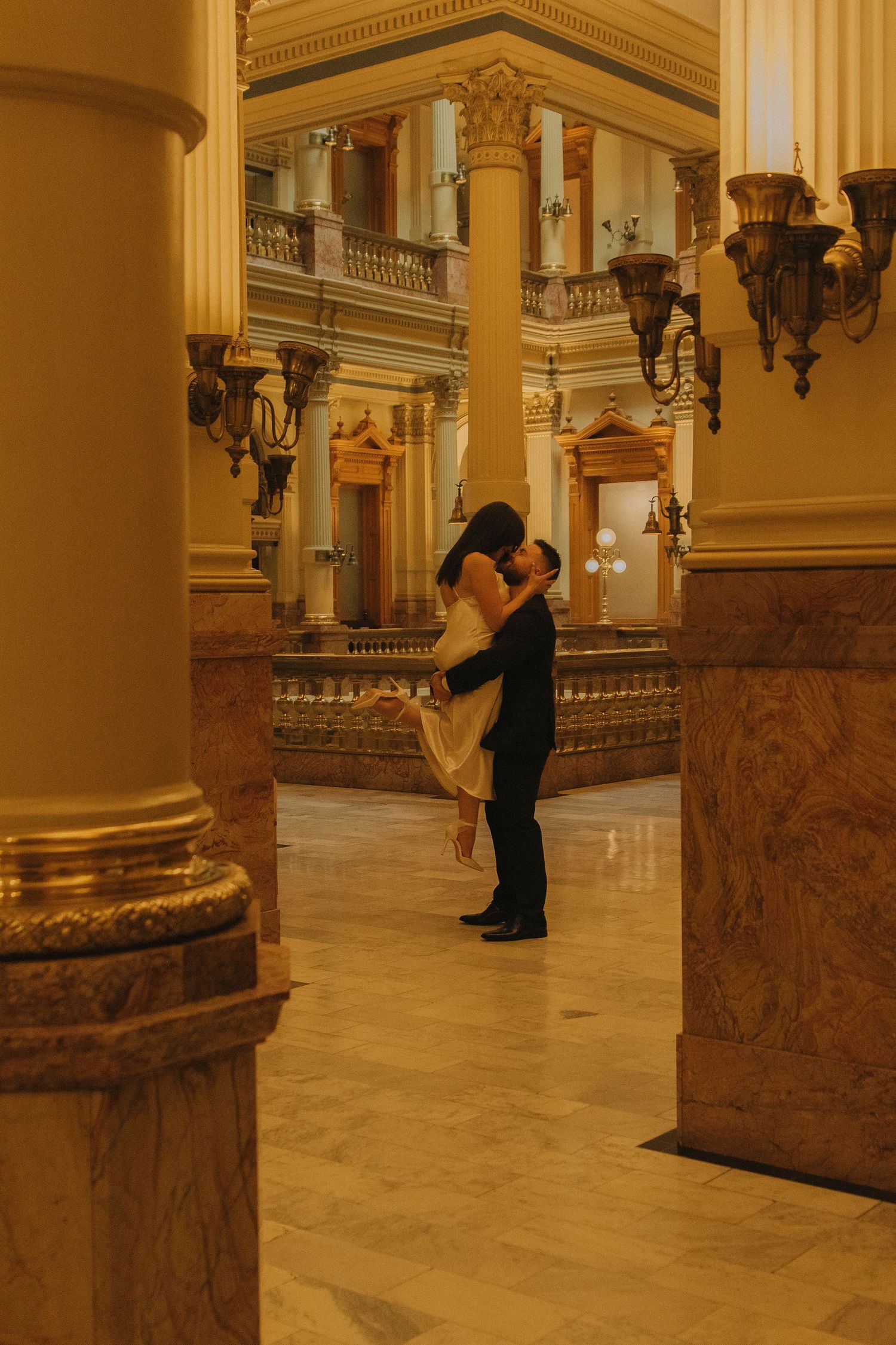 A romantic moment captured in an elegant marble hallway with golden columns and ornate architecture.