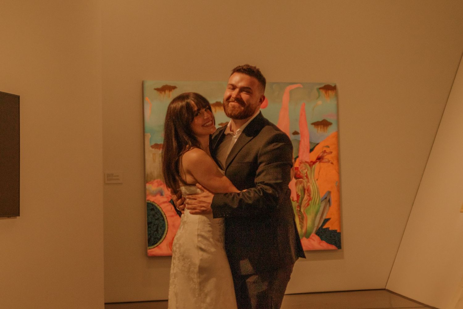 Couple sharing a romantic moment while viewing art in a warmly lit museum gallery.
