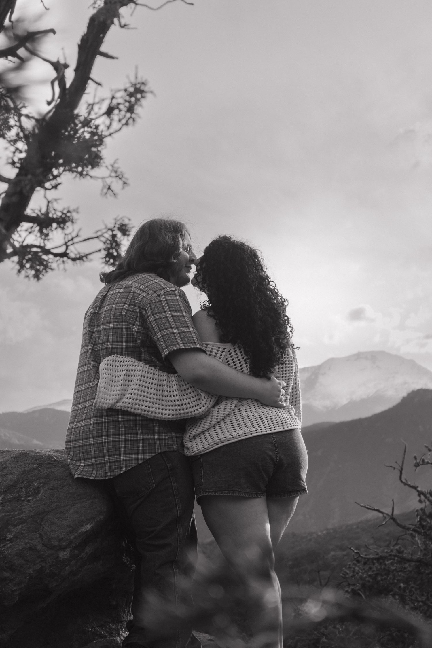 A romantic couple embraces while overlooking mountain views in a black and white photograph.
