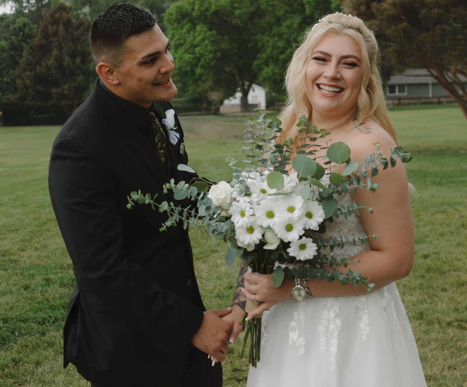 Happy couple sharing joyful moment with white floral bouquet in outdoor setting.