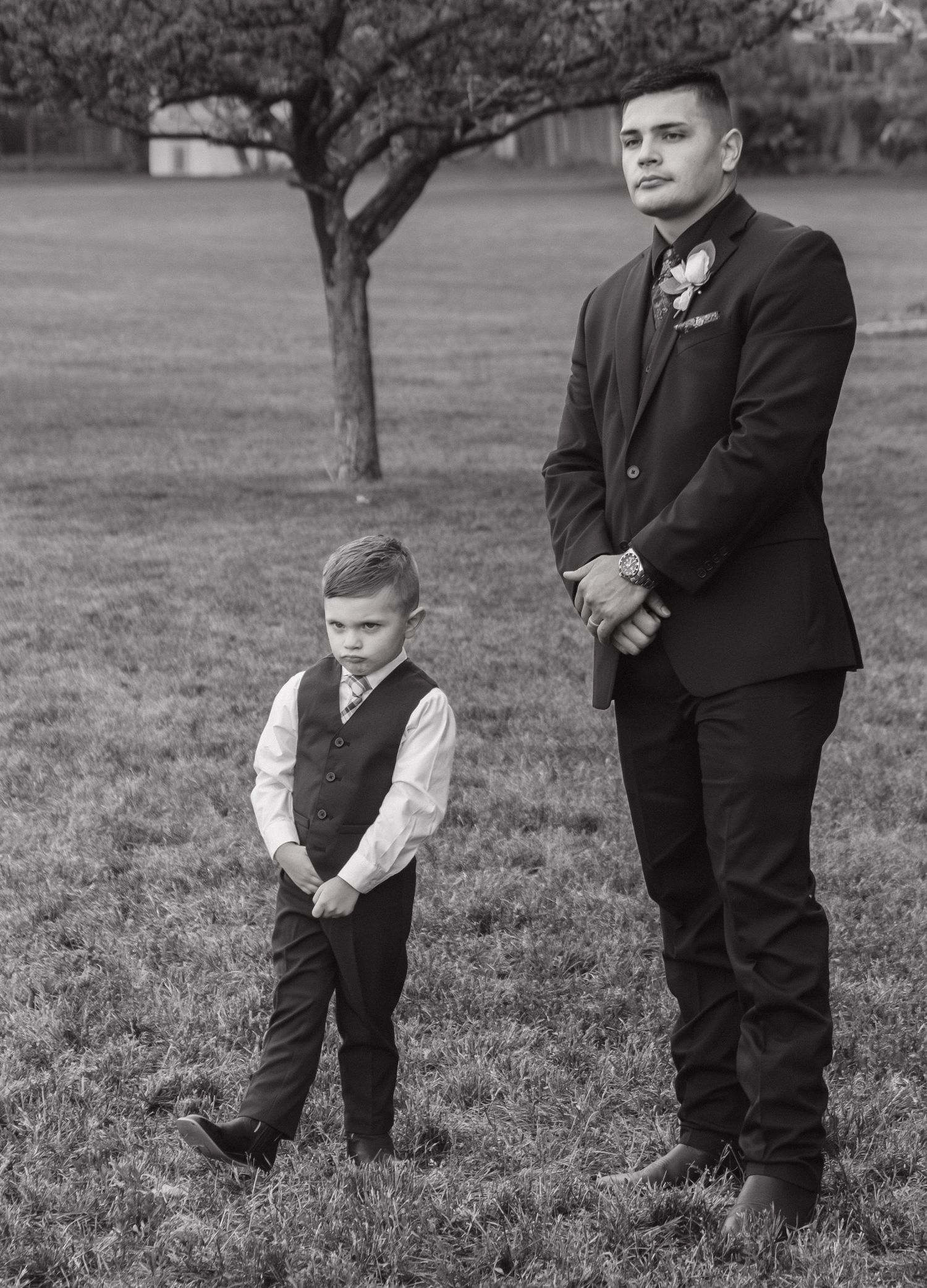Black and white portrait of two formal-dressed attendees standing by a tree.