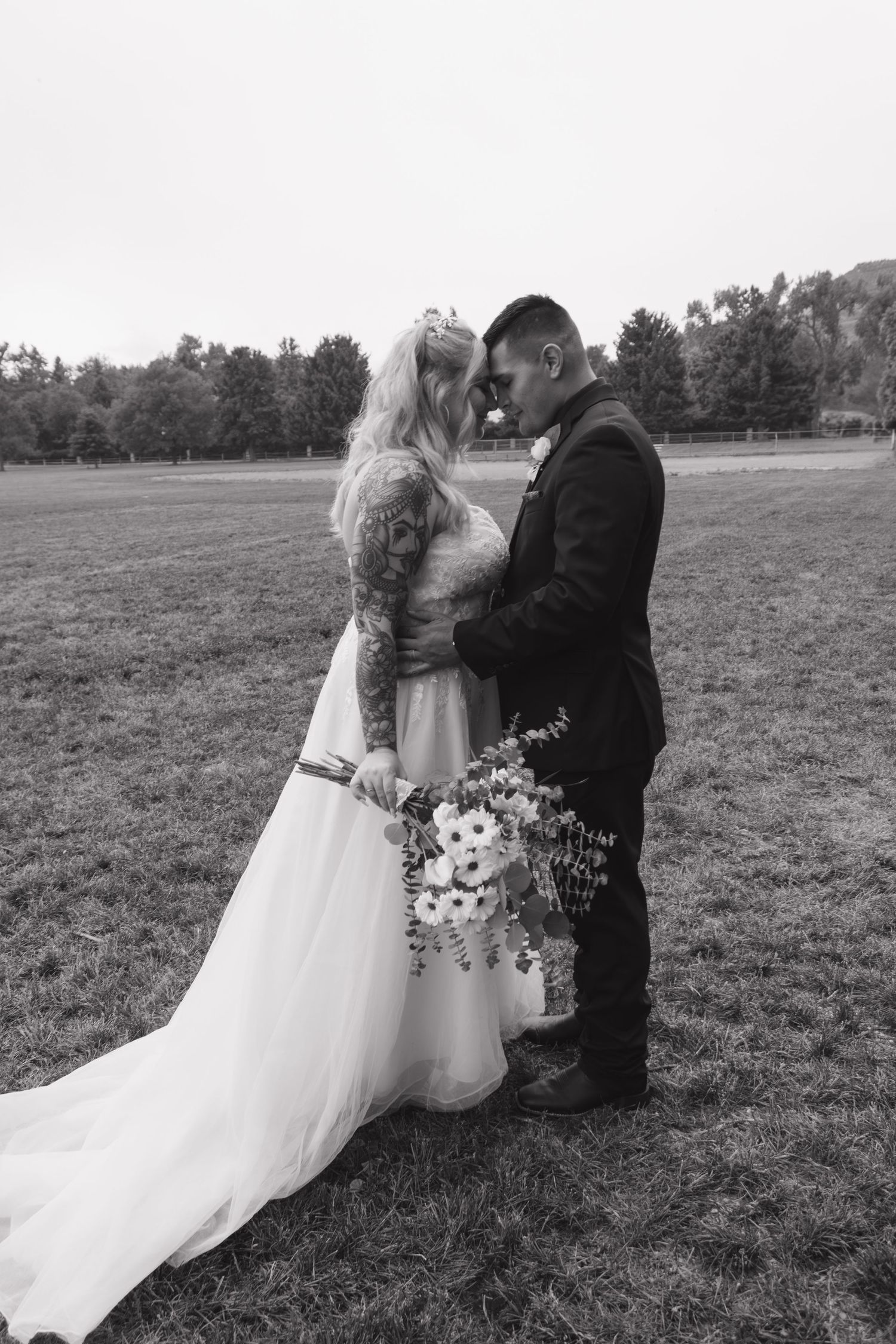 A romantic black and white wedding photo of a couple in a field with the bride holding a bouquet.